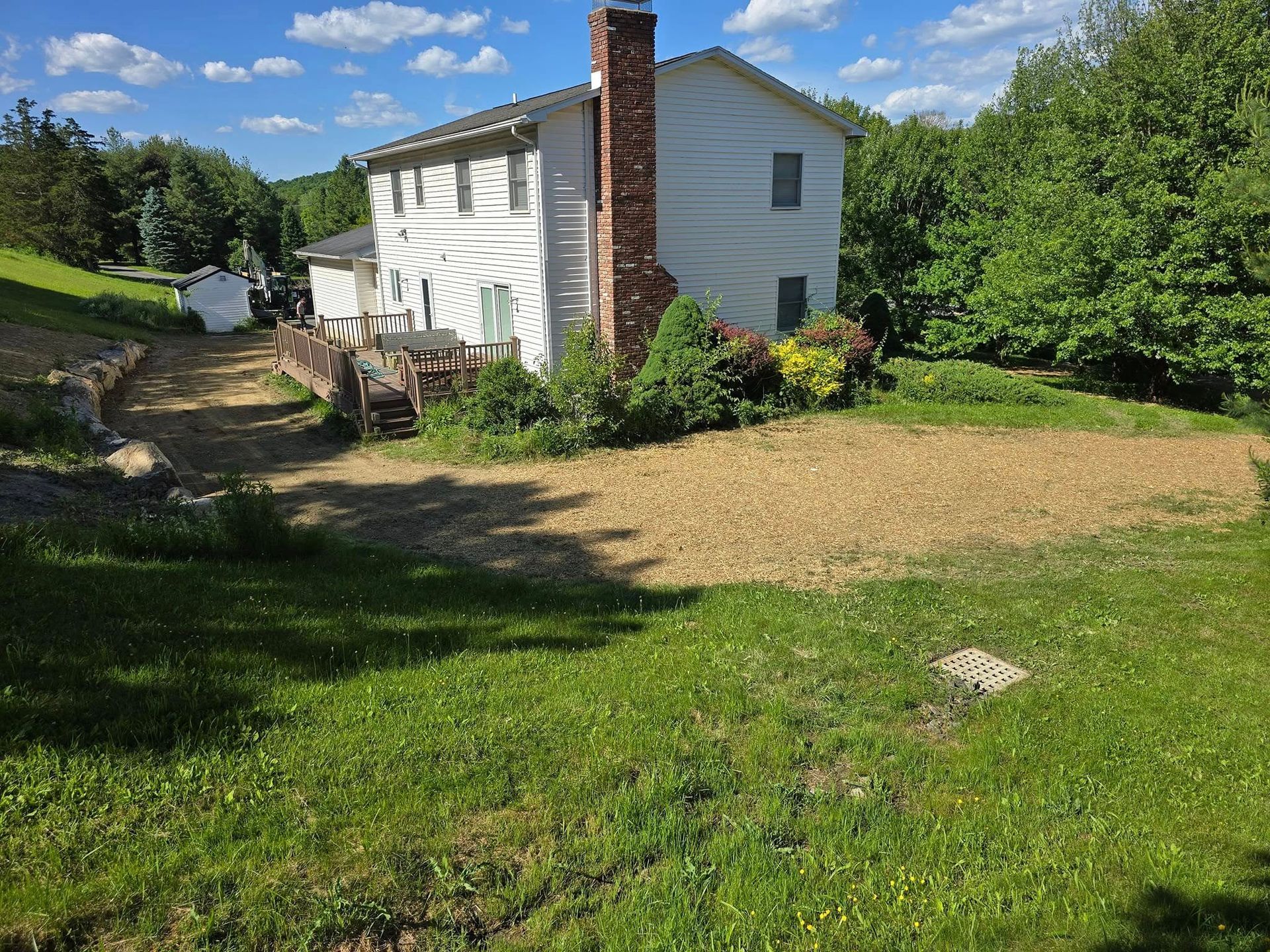 A white house with a brick chimney is surrounded by grass and trees.