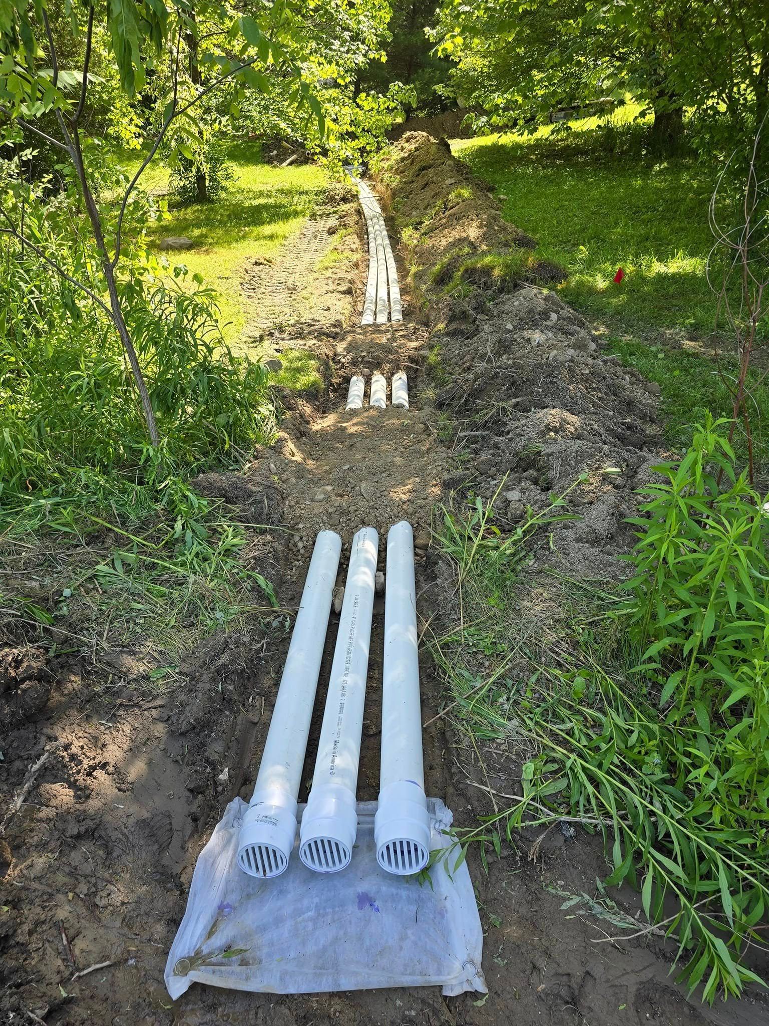 Three white pipes are sitting in the dirt next to a tree.