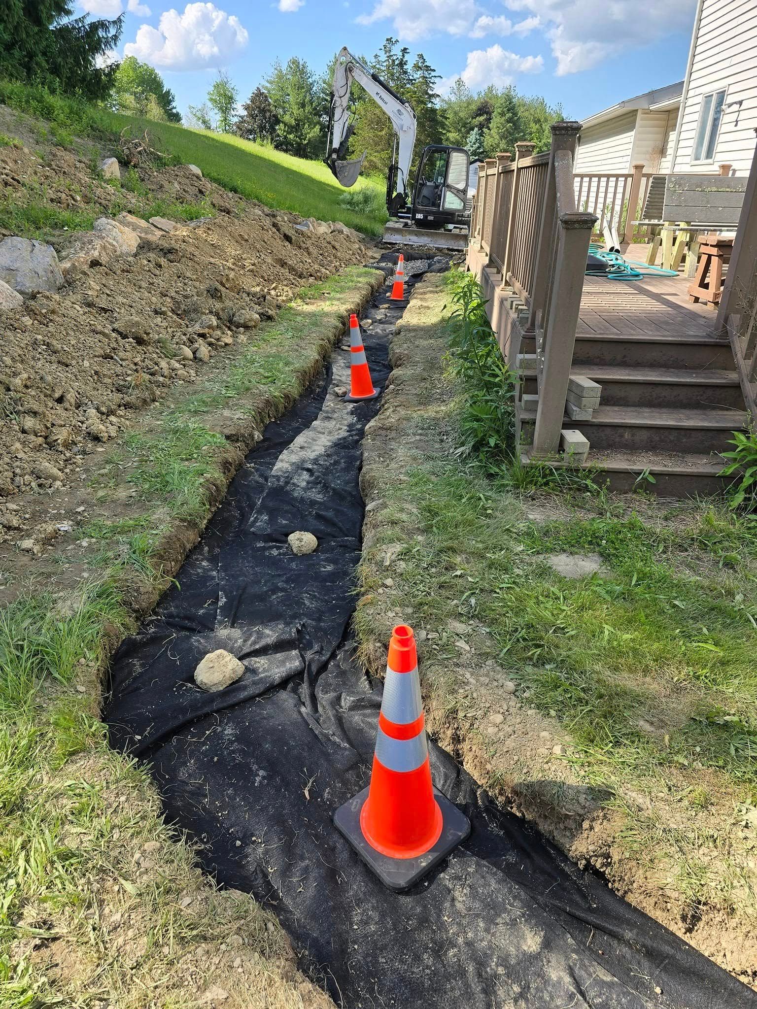 A row of orange and white traffic cones sitting on top of a dirt path next to a house.