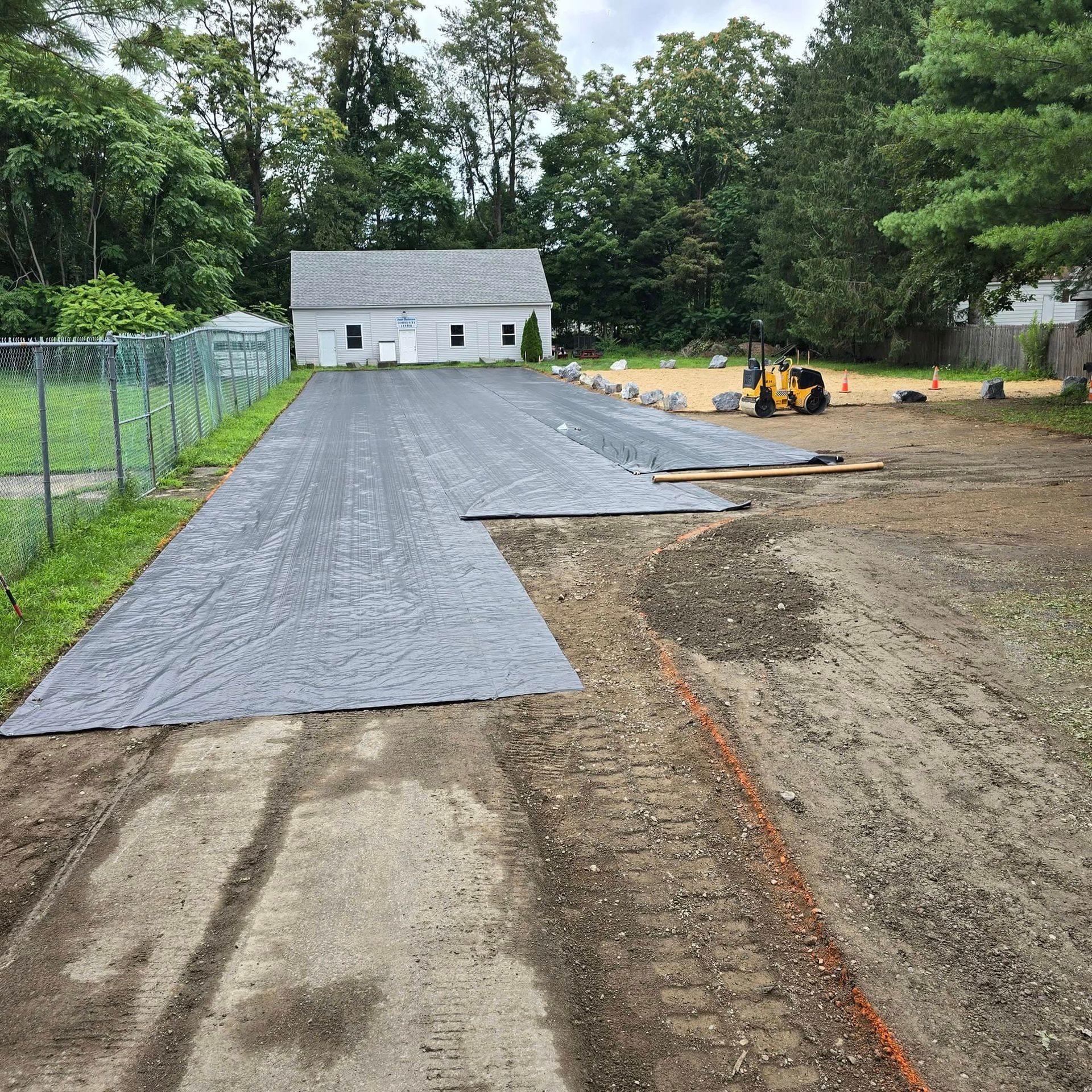 A tractor is driving down a dirt road next to a house.