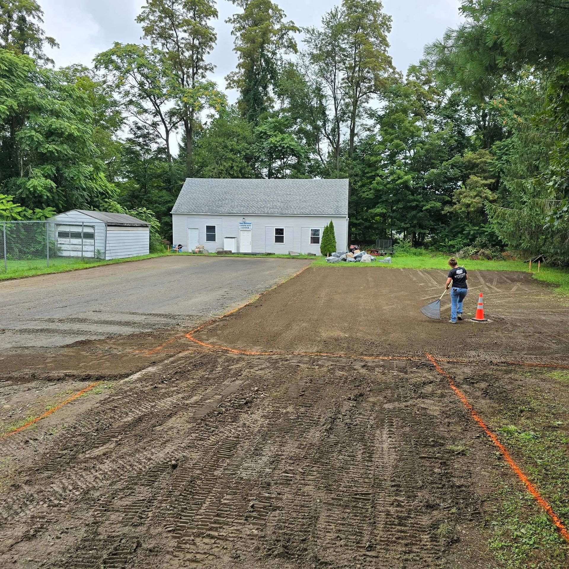 A man is standing in a dirt field in front of a house.