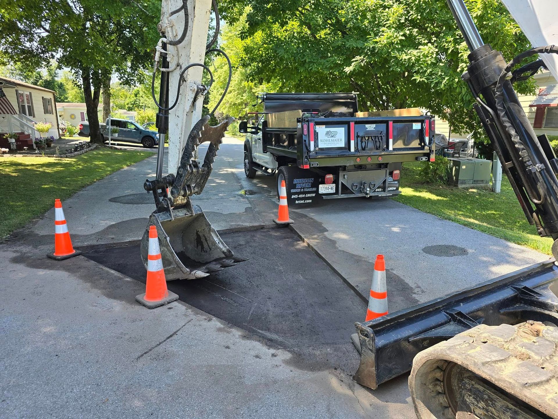An excavator is digging a hole in the road next to a dump truck.