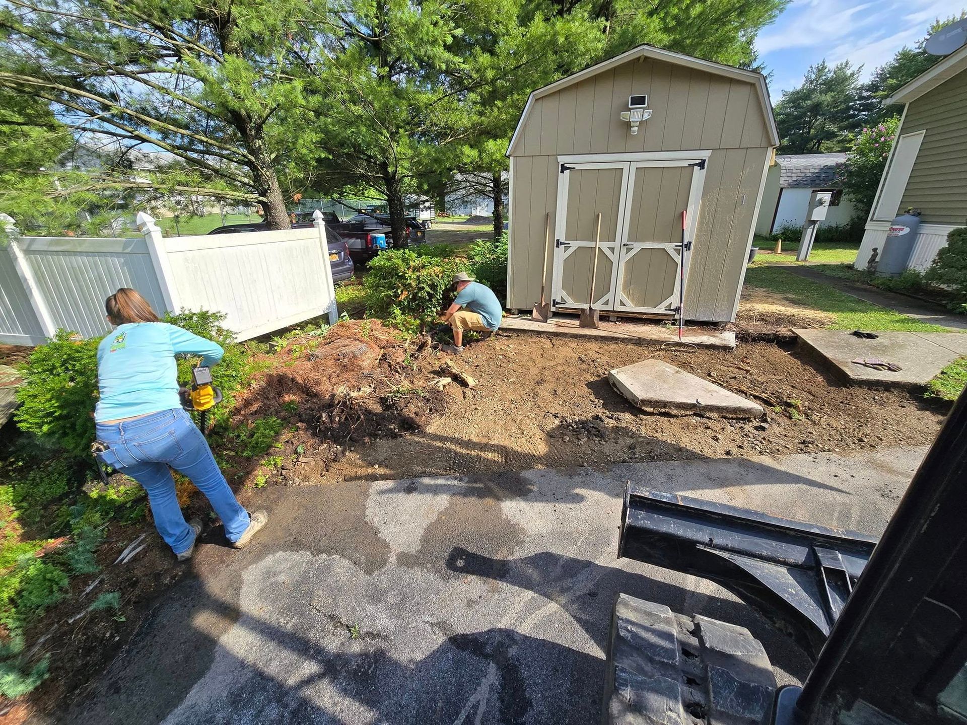 A woman is digging a hole in the ground in front of a shed.