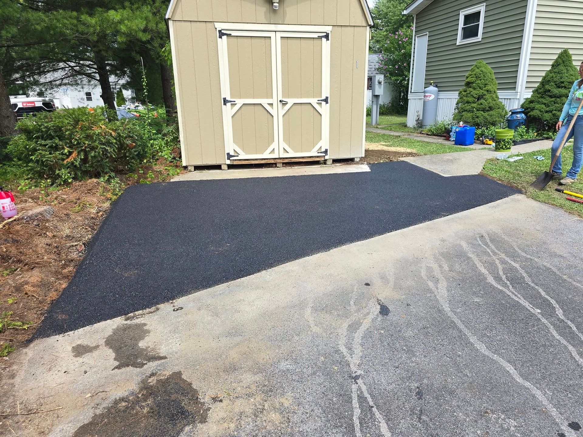 A shed is sitting in the middle of a driveway next to a house.