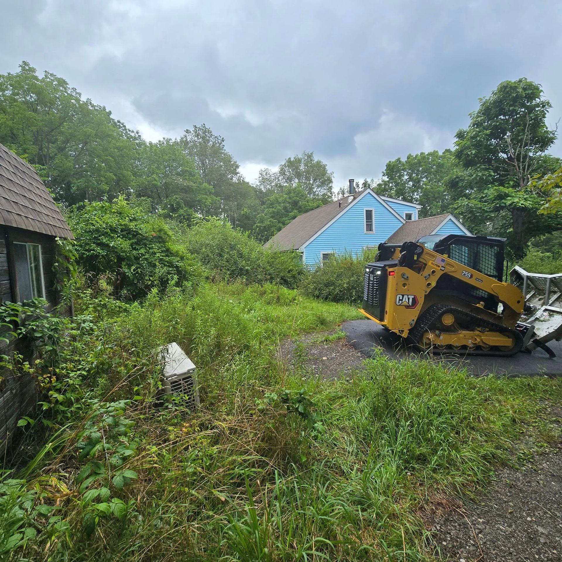 A yellow bulldozer is parked in a grassy field in front of a blue house.