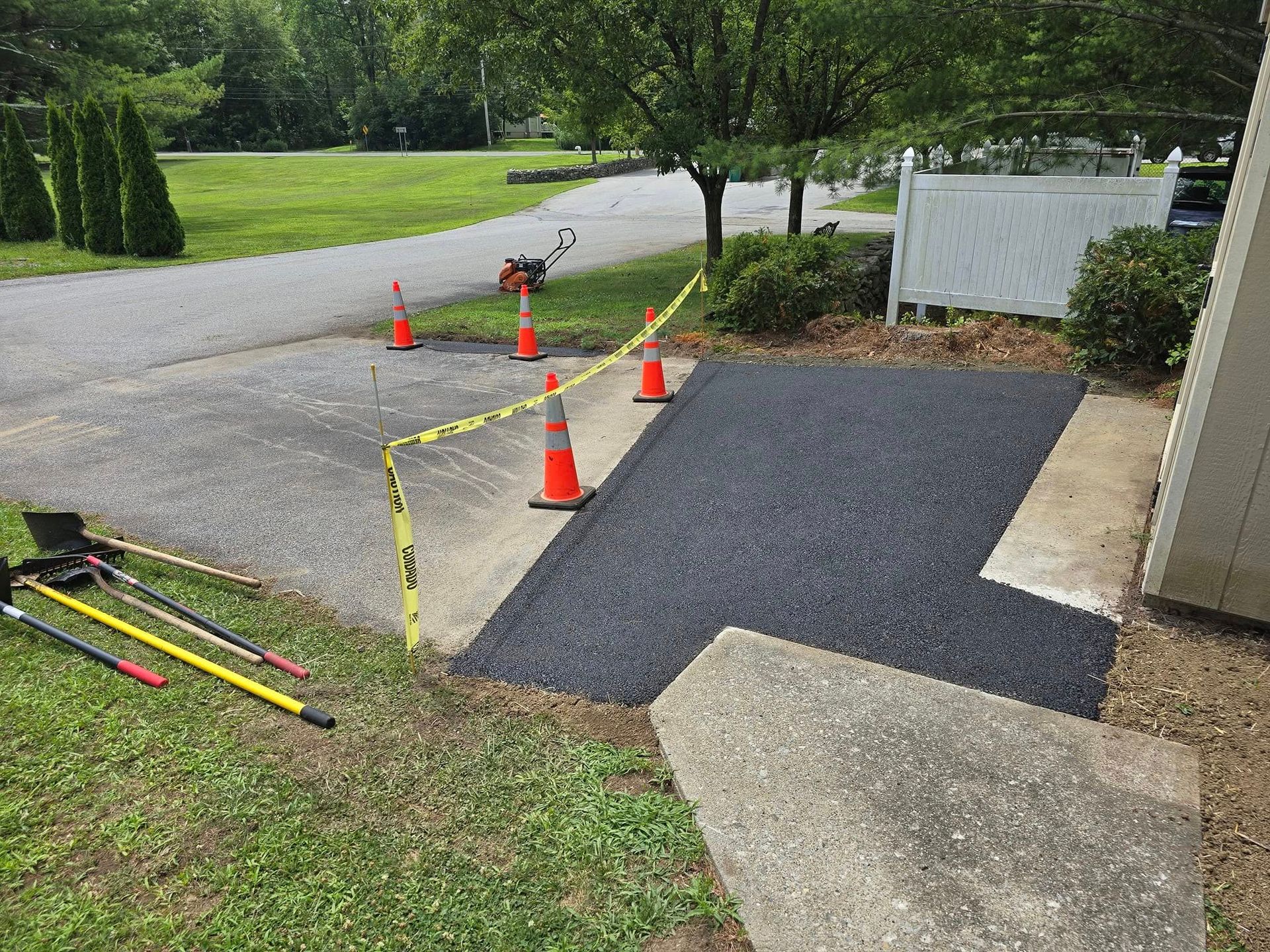 A driveway is being paved with asphalt and orange cones.