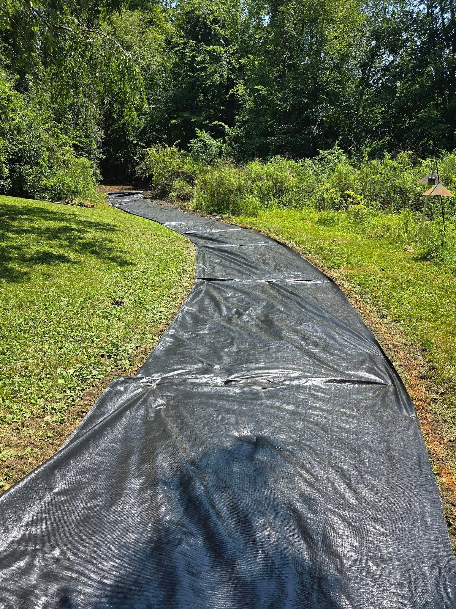 A black tarp is covering a path in the grass.