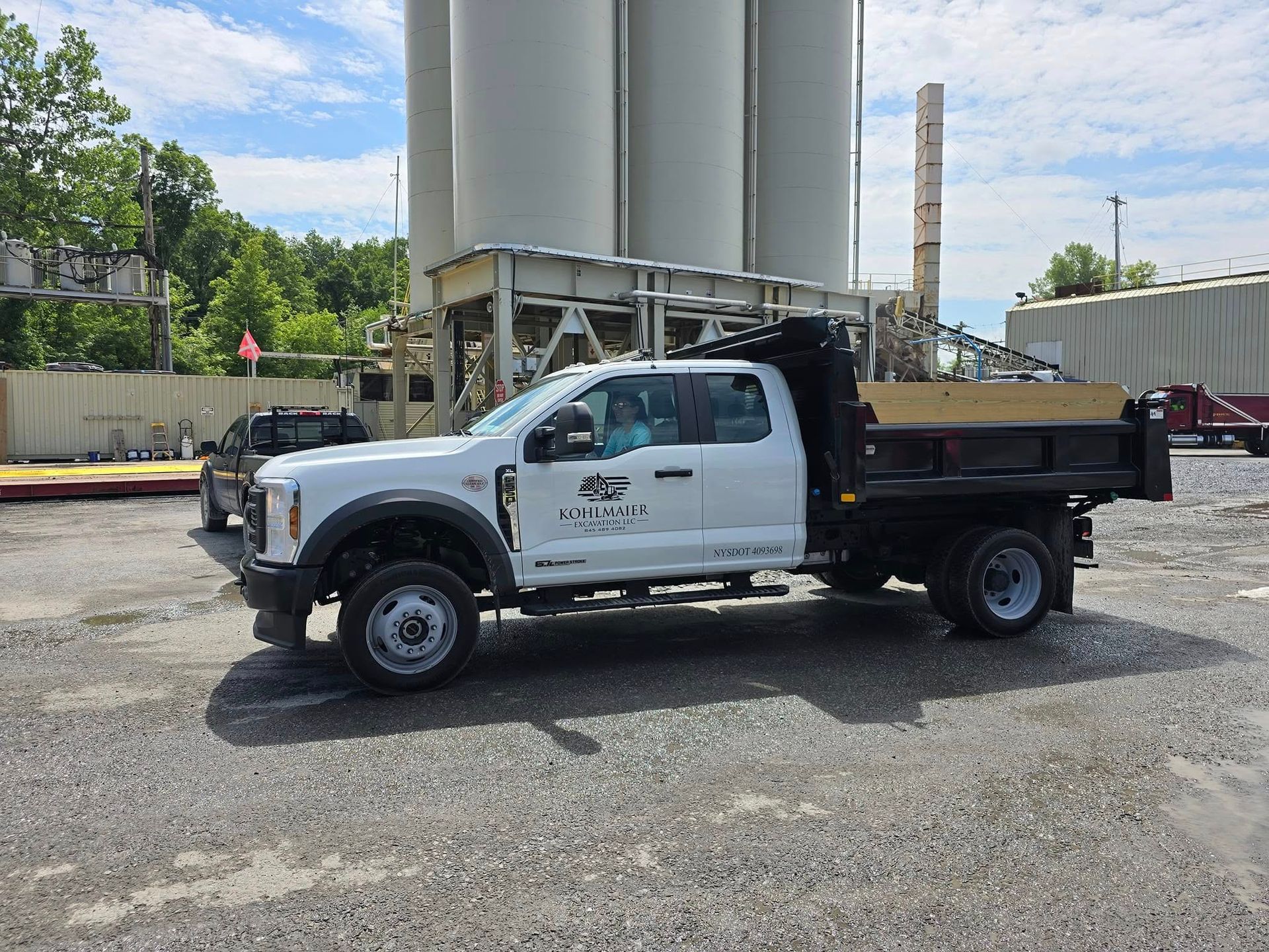 A white dump truck is parked in a gravel lot in front of a cement plant.