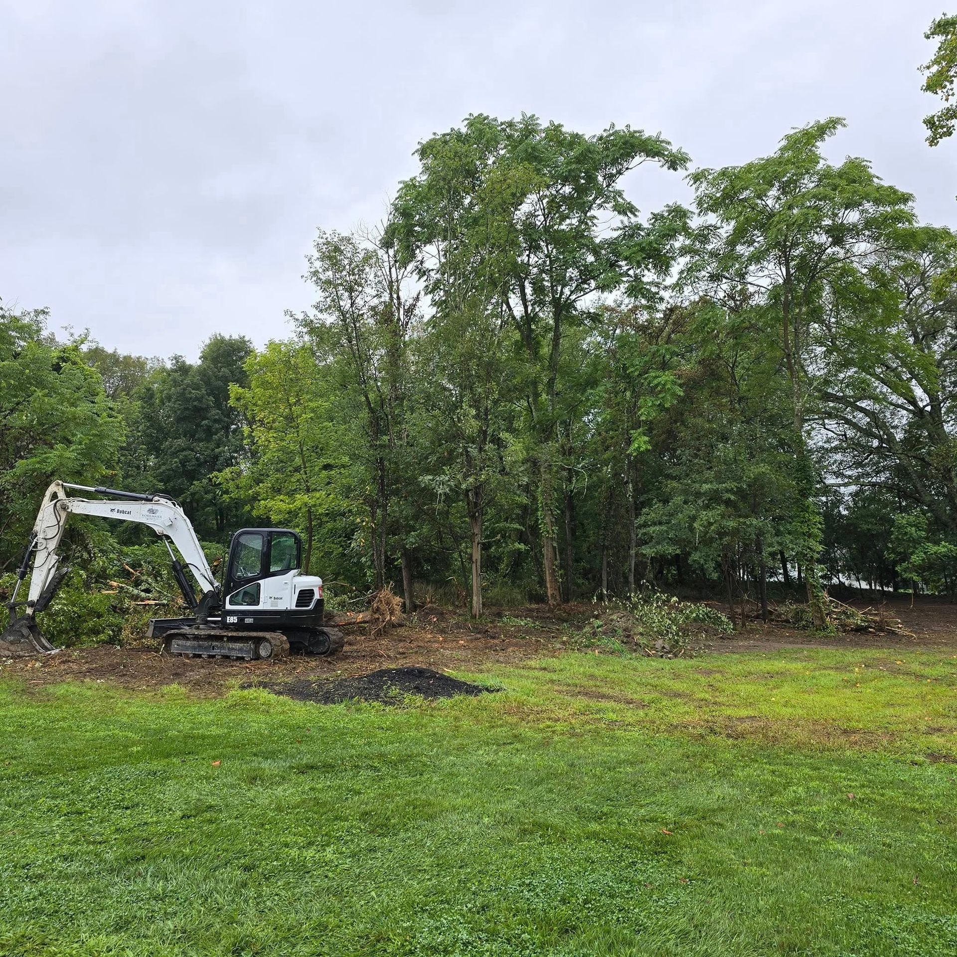 A white and black excavator is working in a grassy field.