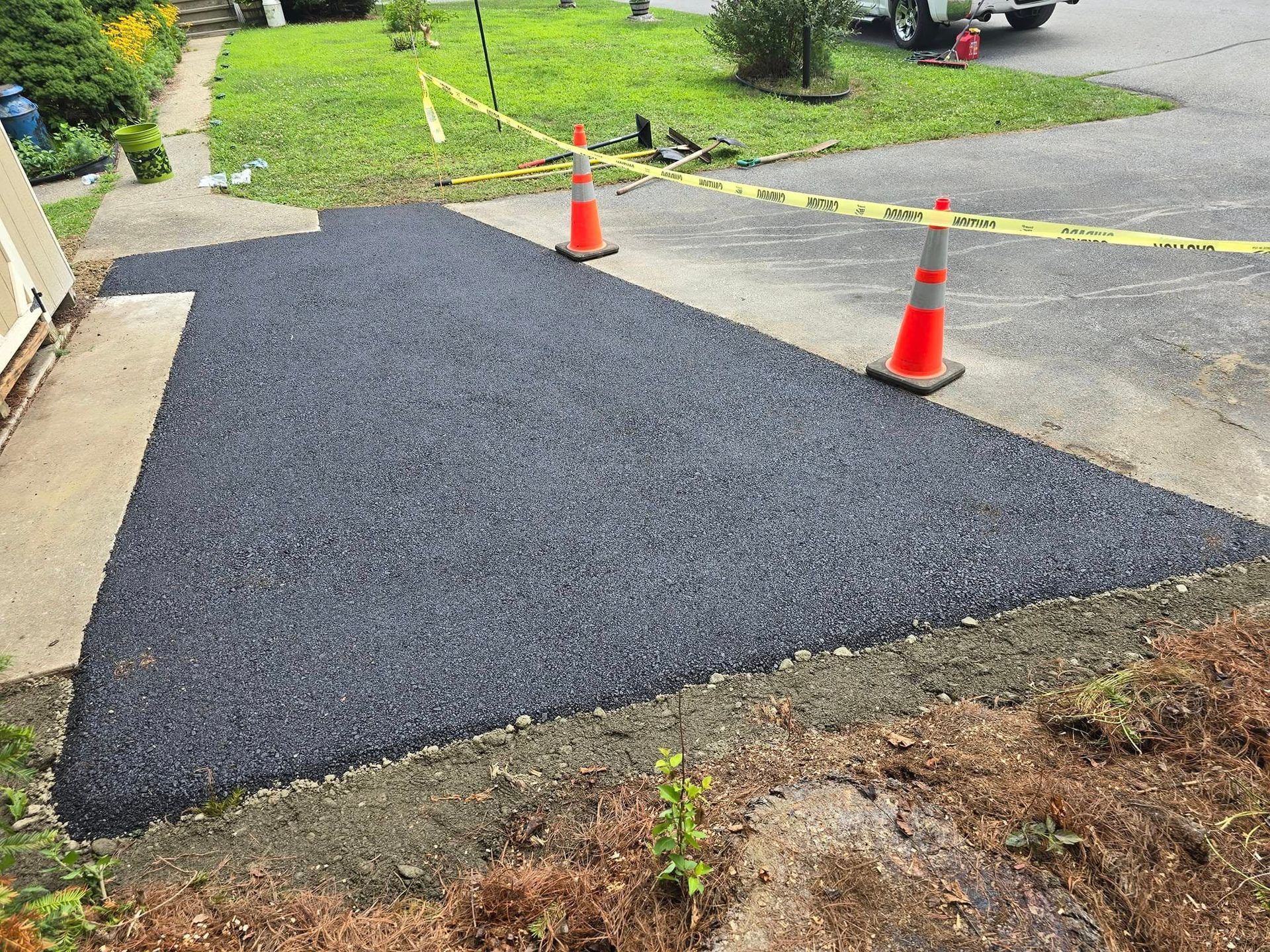 Two orange and white traffic cones are sitting on top of a newly paved driveway.