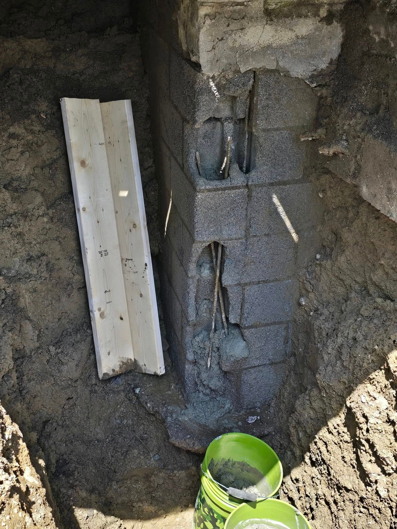 A bucket of concrete is sitting next to a brick wall.