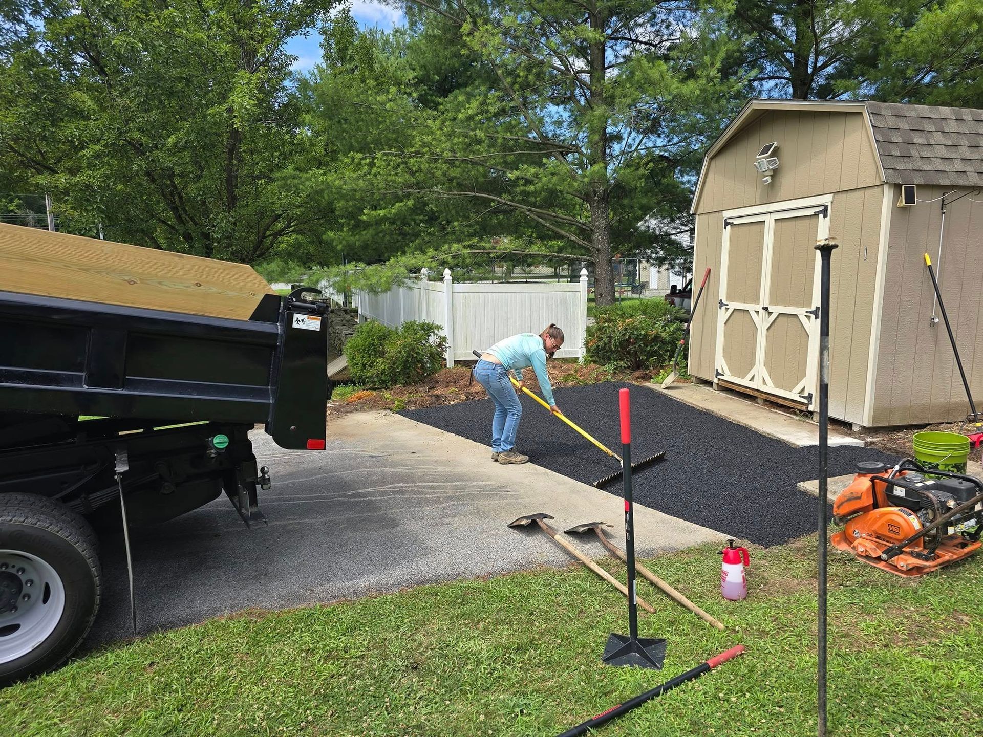 A man is laying asphalt in a driveway next to a dump truck.
