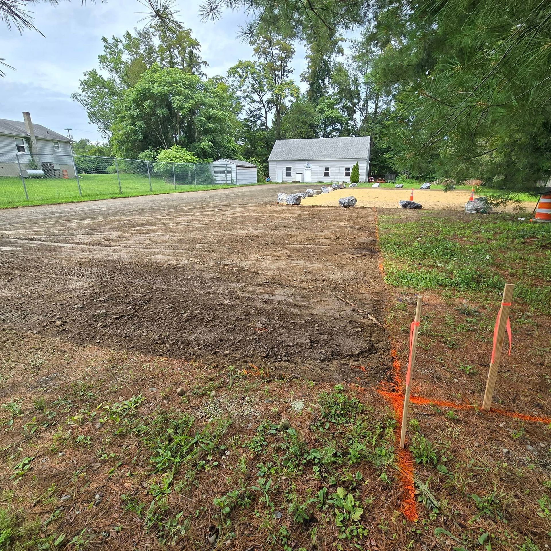 A dirt field with a house in the background and a fence in the foreground.