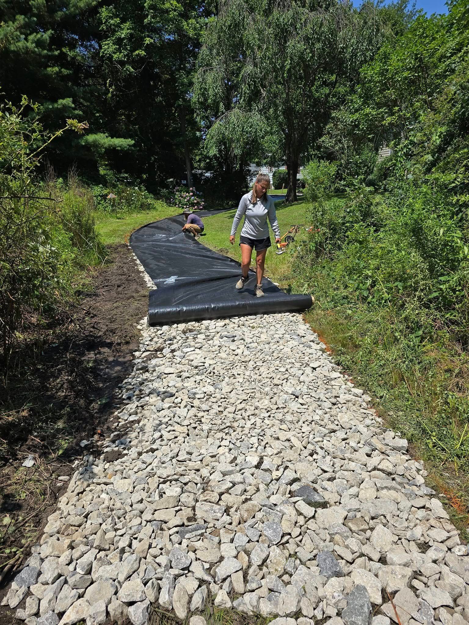 A woman is walking down a gravel path in the woods.