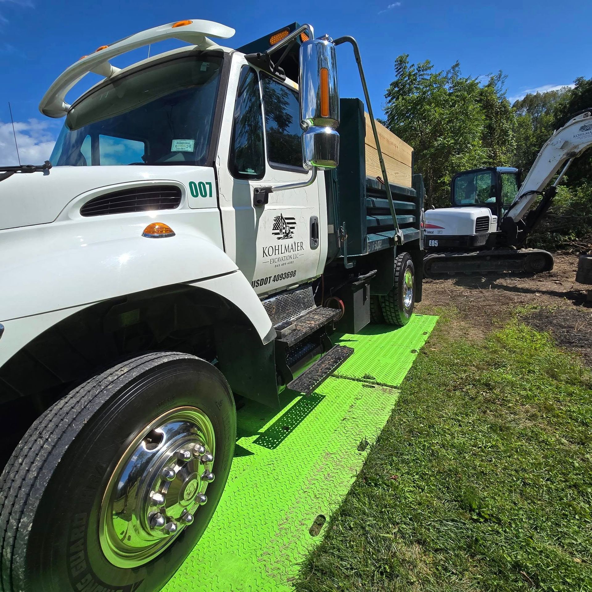 A white truck is parked on a green mat next to an excavator.