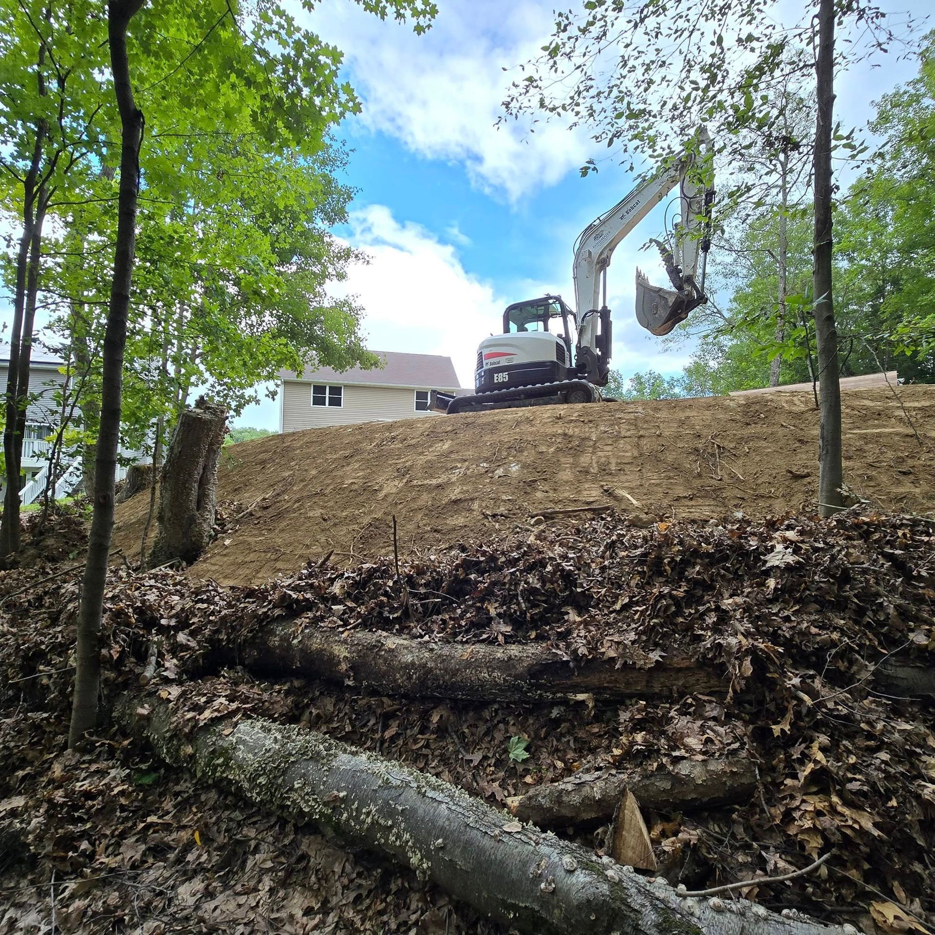 An excavator is working on a dirt hill near a house.