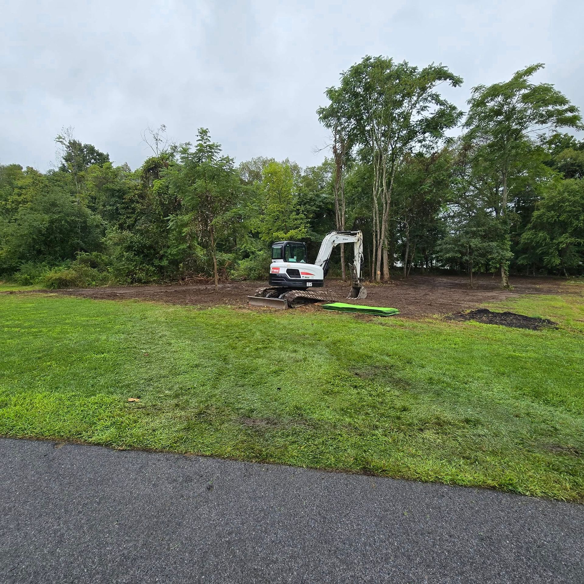 A white excavator is sitting in the middle of a grassy field.