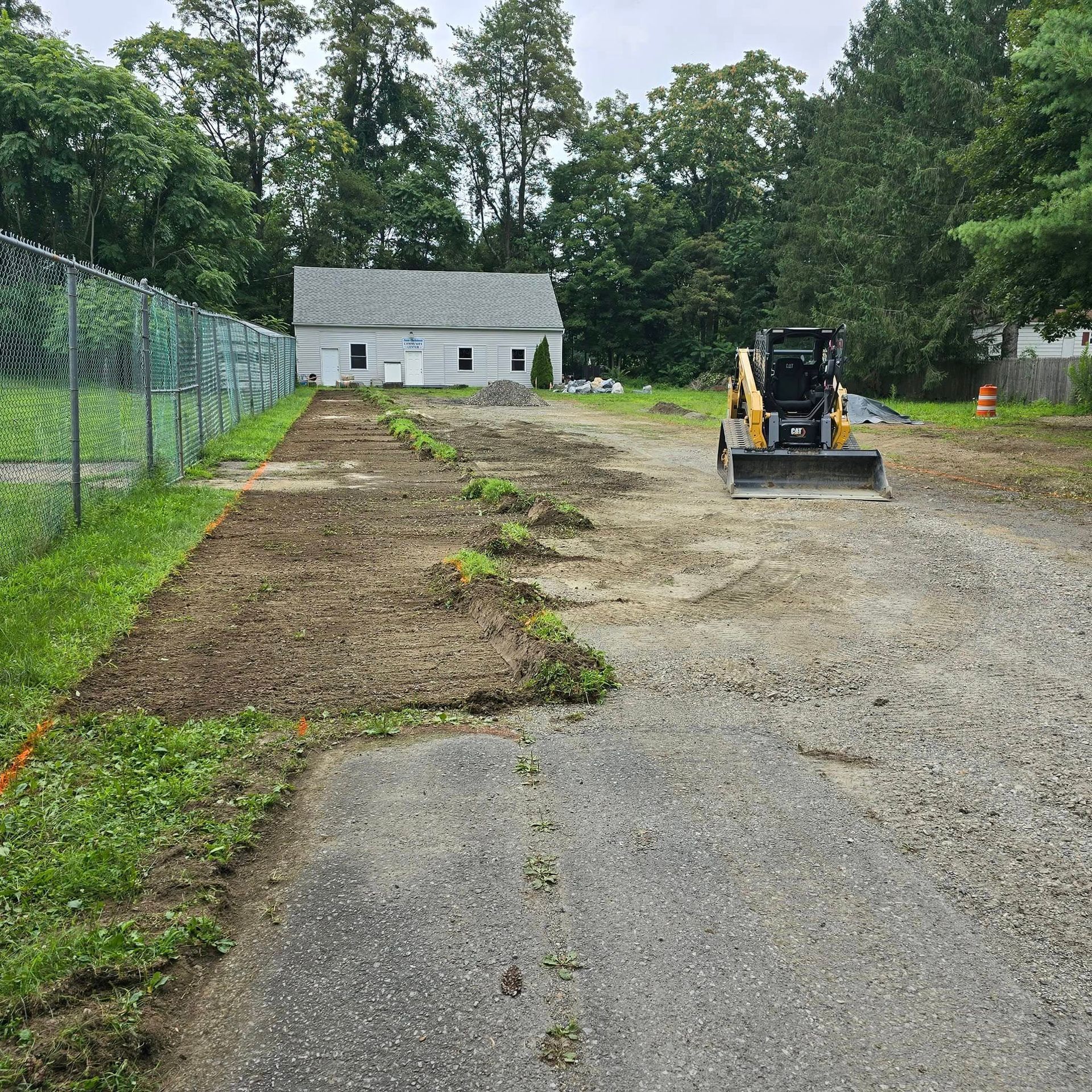 A bulldozer is driving down a dirt road next to a house.