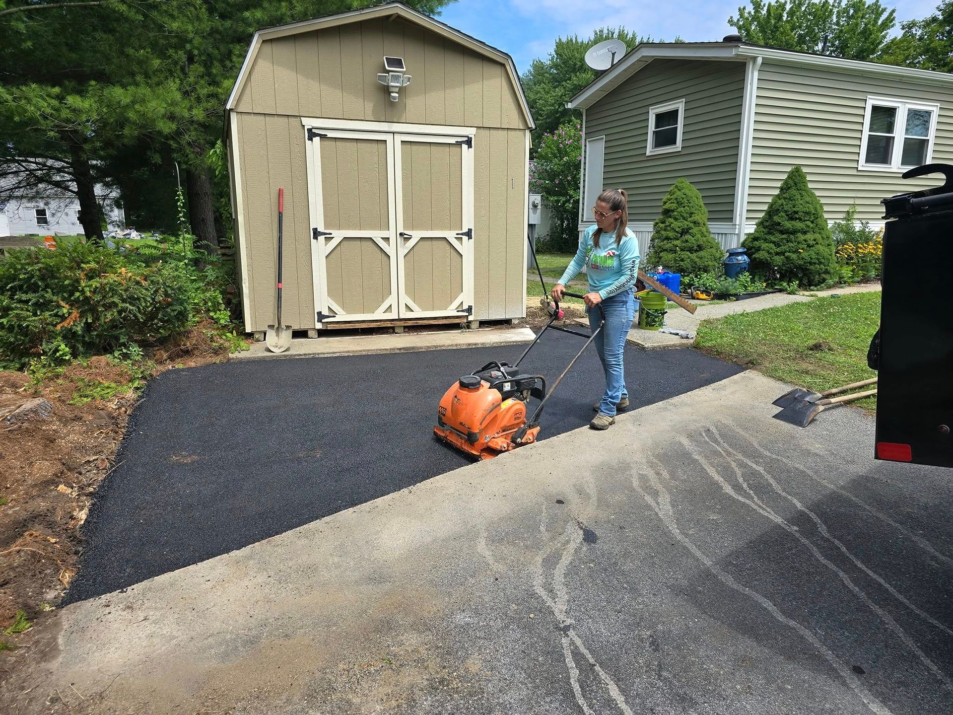 A woman is working on a driveway in front of a shed.