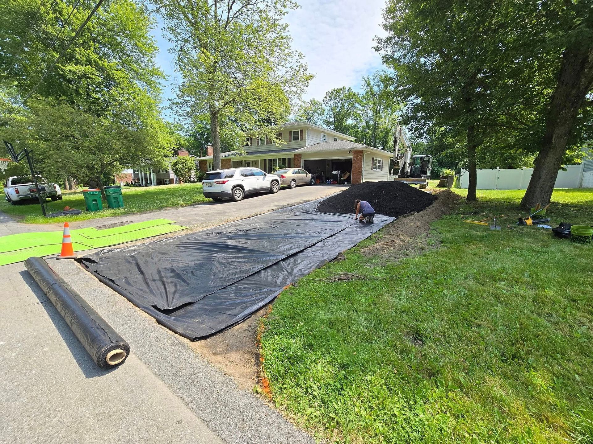 A roll of black tarp is sitting on the side of a road in front of a house.