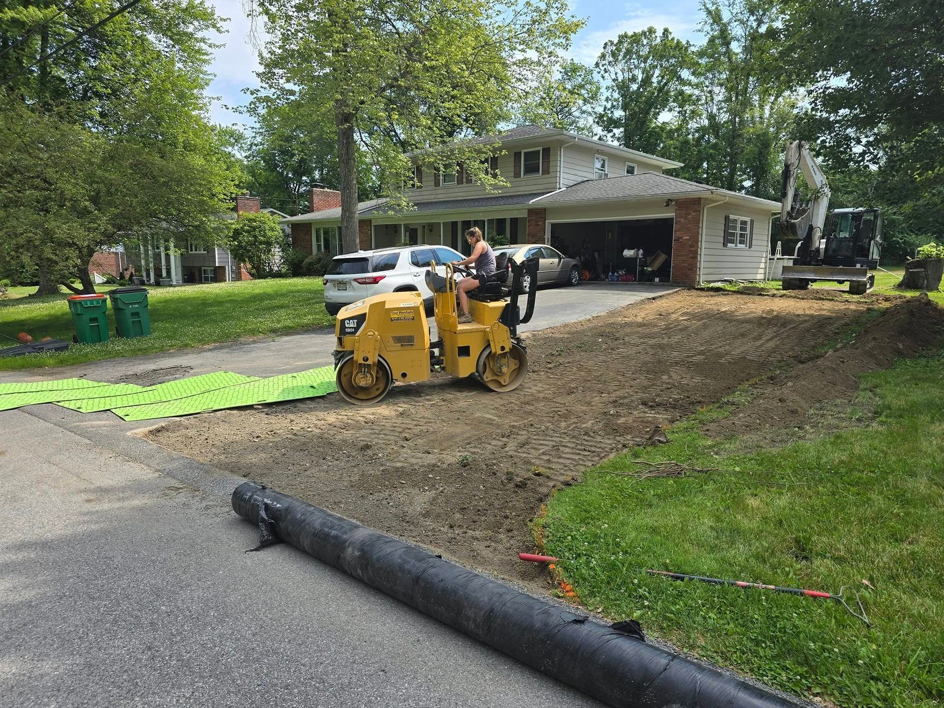 A yellow tractor is driving down a dirt road in front of a house.