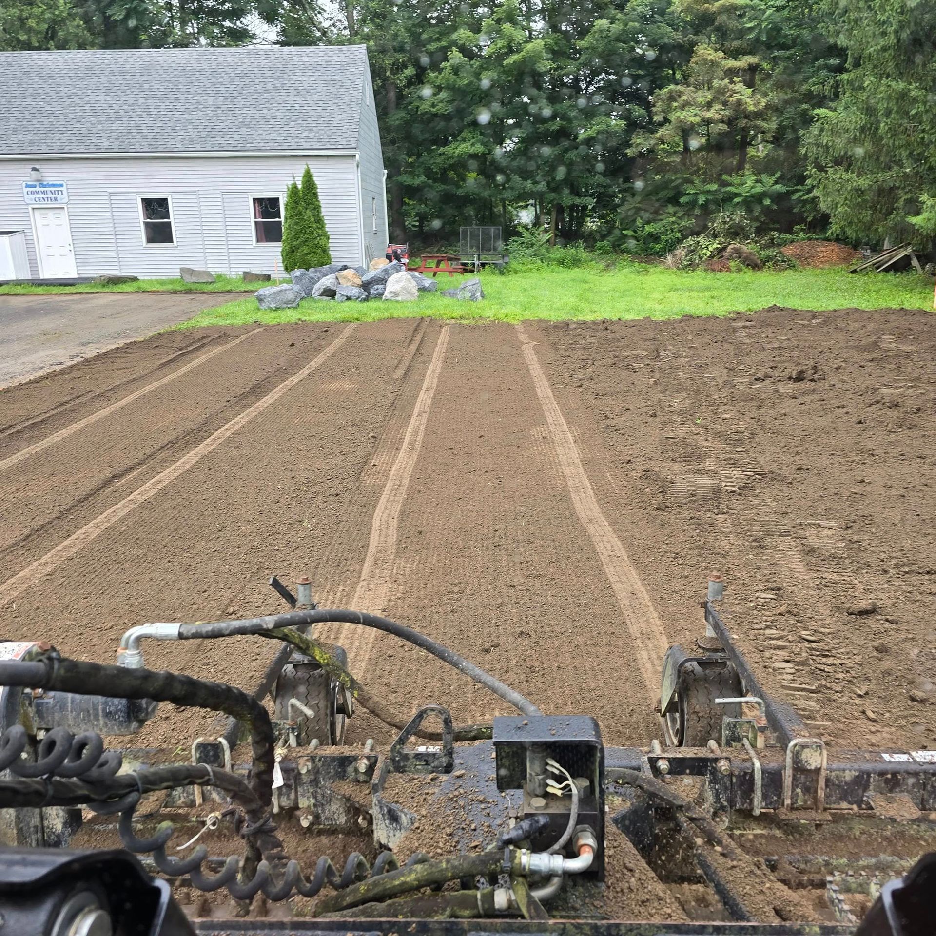 A tractor is plowing a field with a house in the background