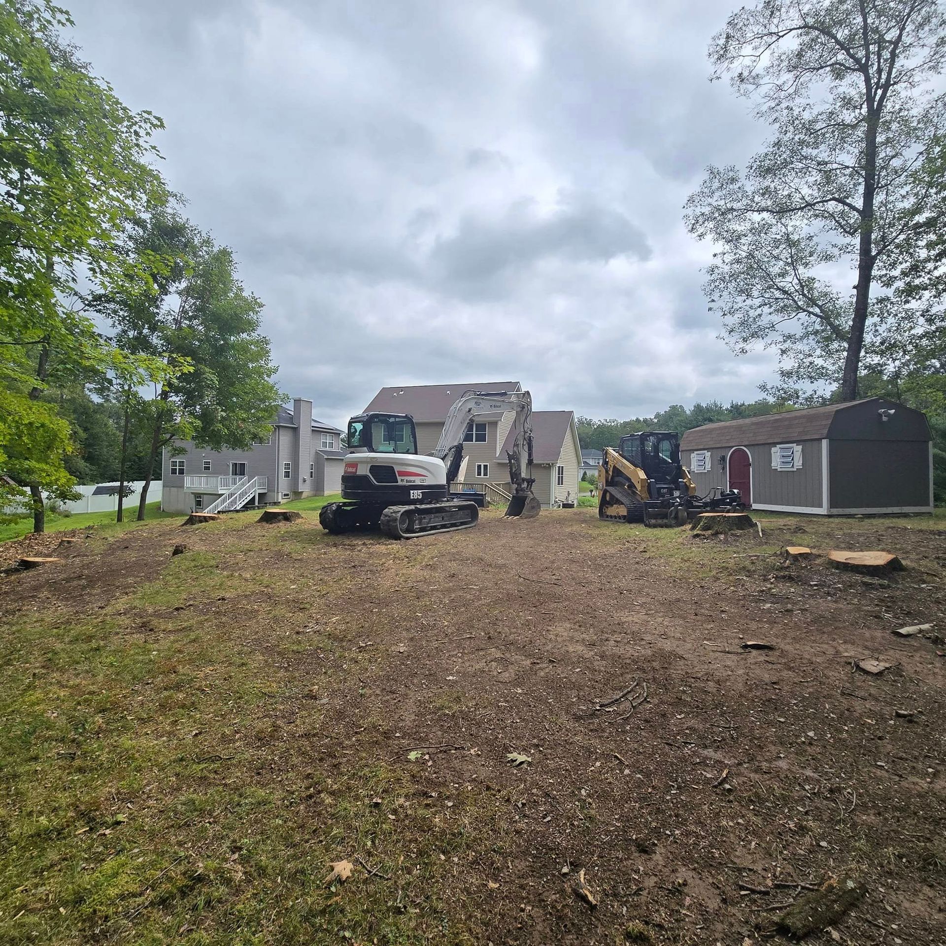 A couple of tractors are parked in a dirt field in front of a house.