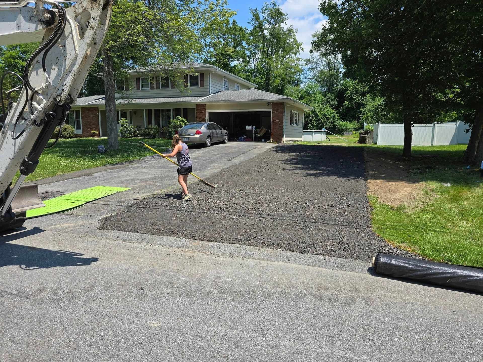 A woman is raking a driveway in front of a house.
