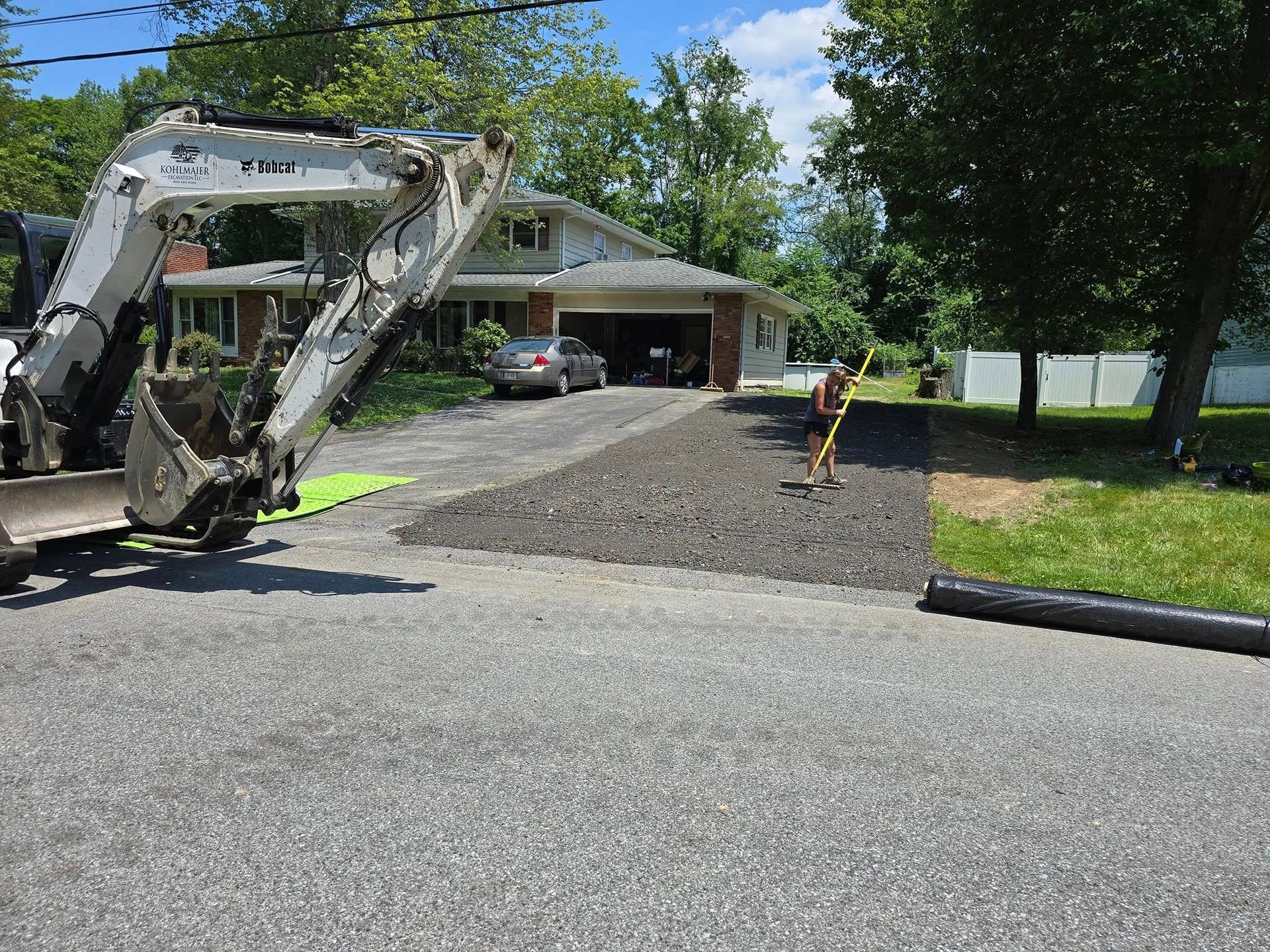 An excavator is working on a driveway in front of a house.