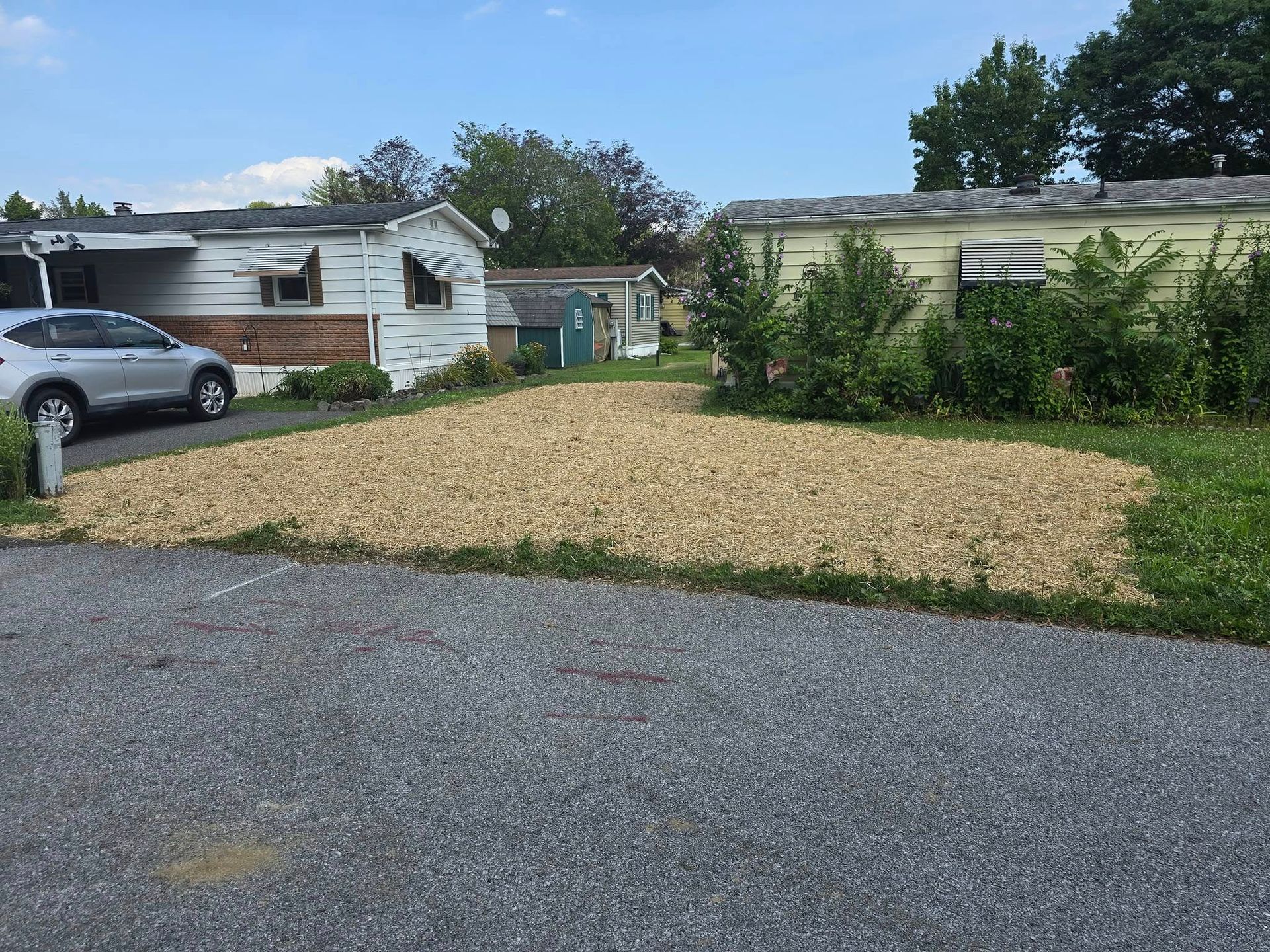 A silver car is parked in a driveway in front of a mobile home.