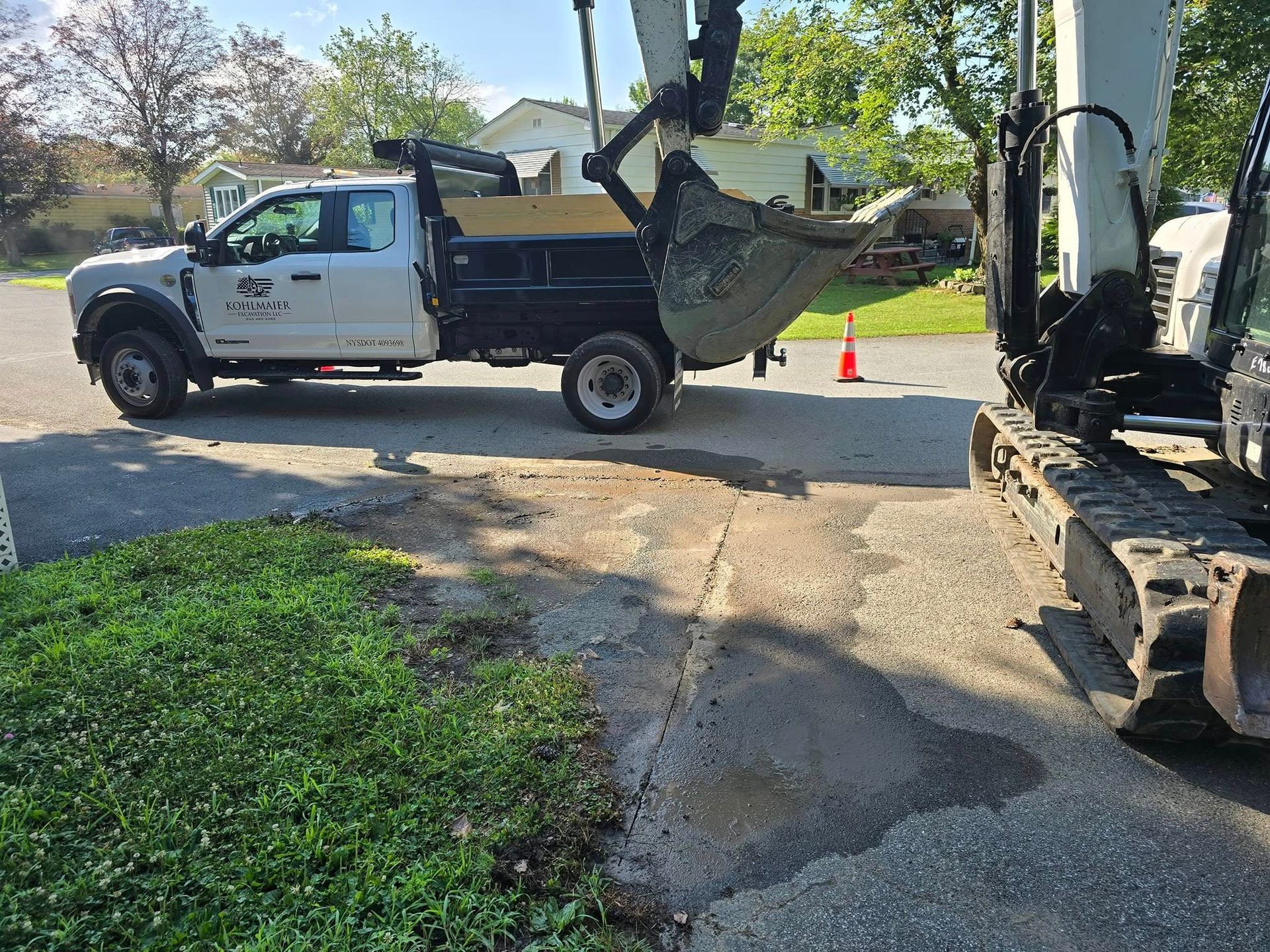 A white truck is parked on the side of the road next to an excavator.
