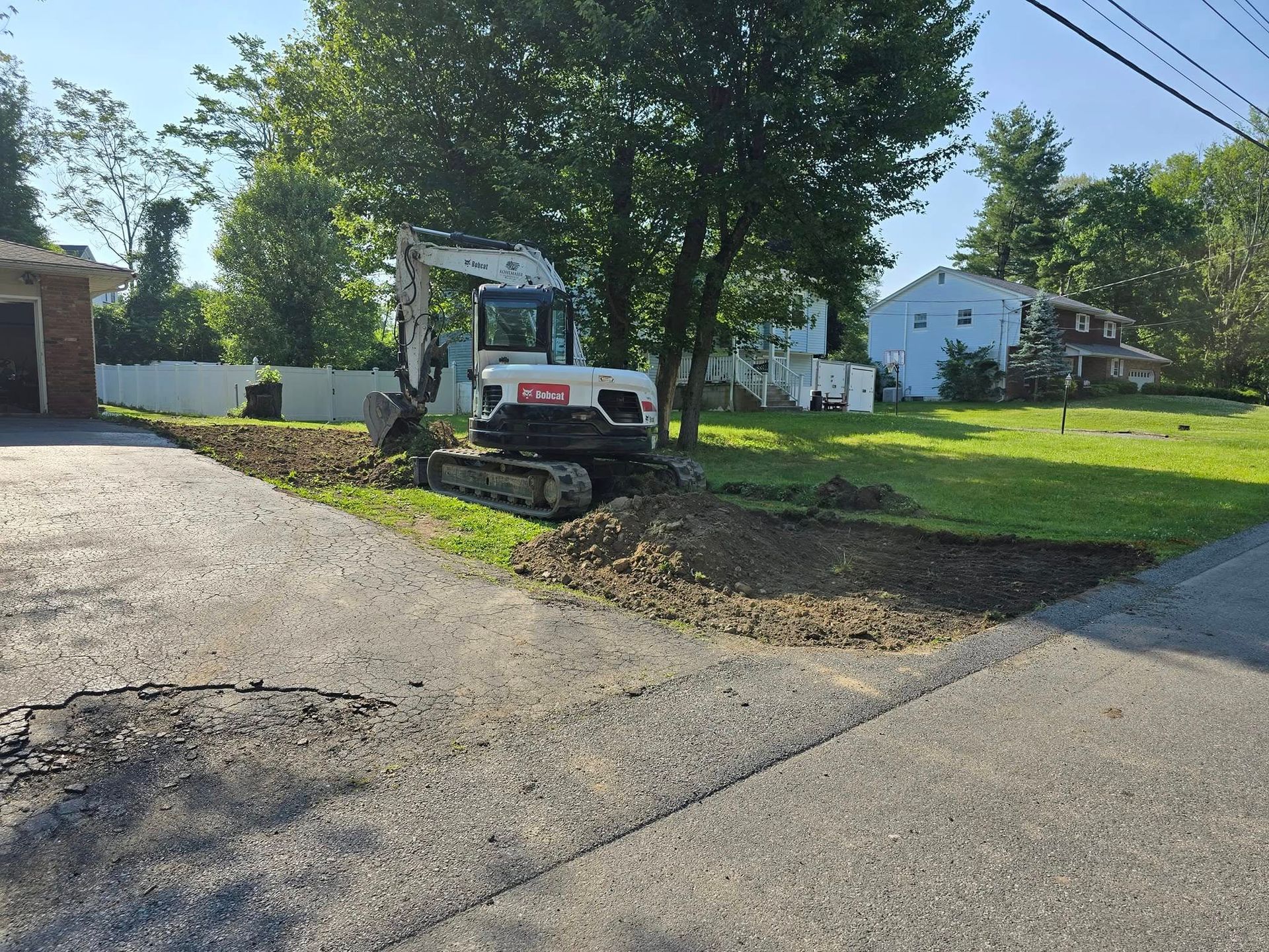 A bobcat excavator is digging a hole in a driveway.