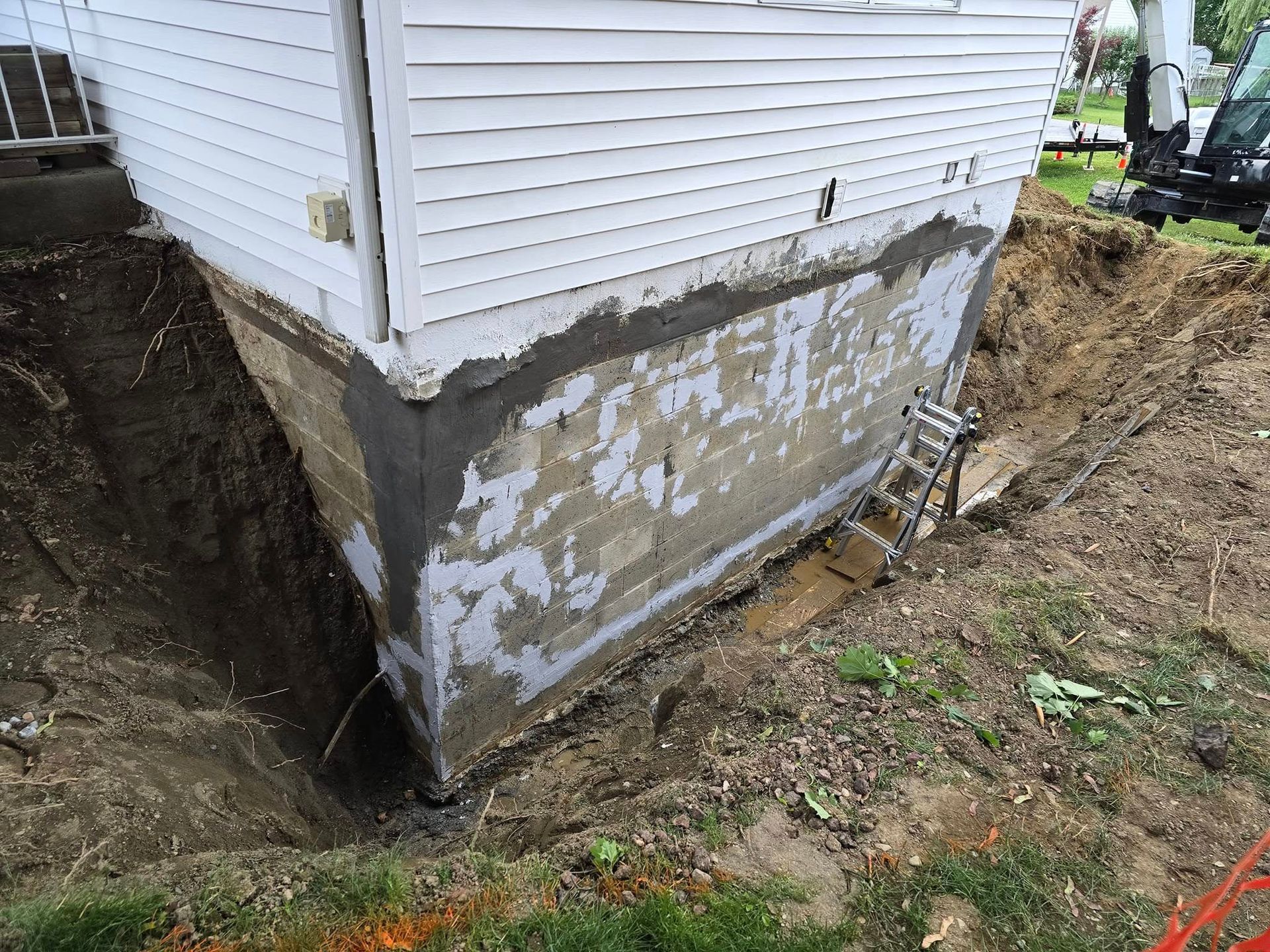 A white house with a ladder in the dirt next to it.