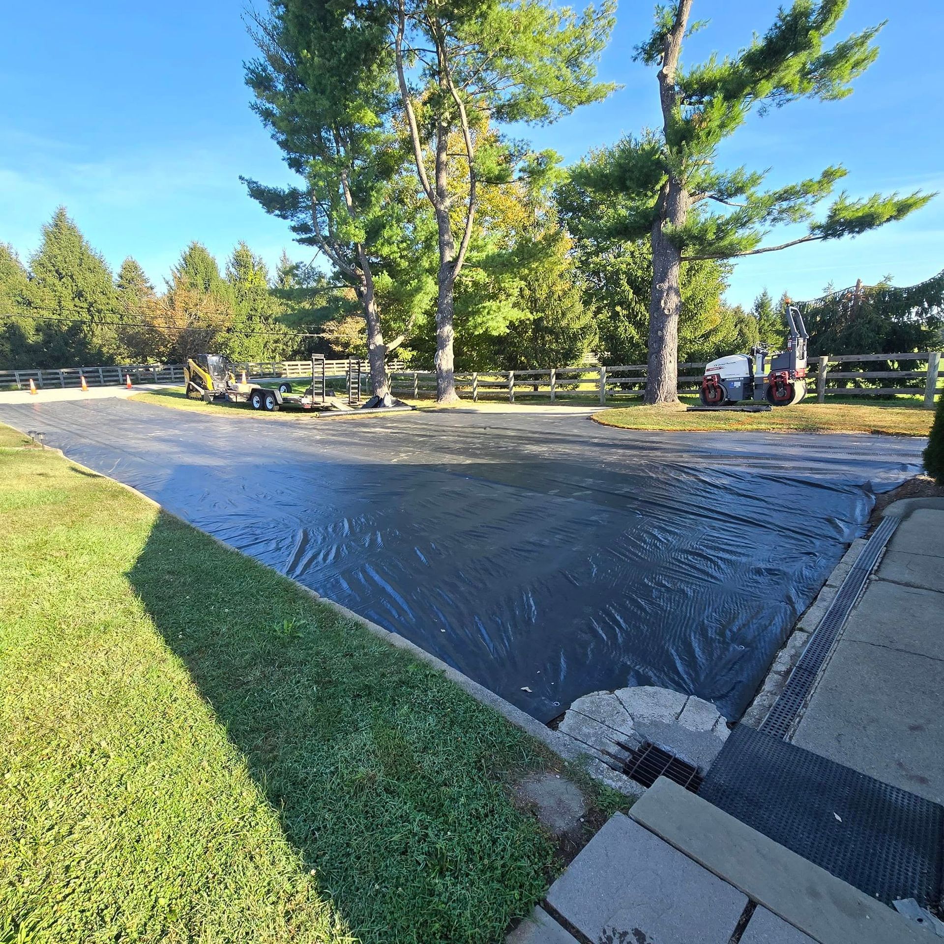 A black tarp is covering a parking lot with trees in the background