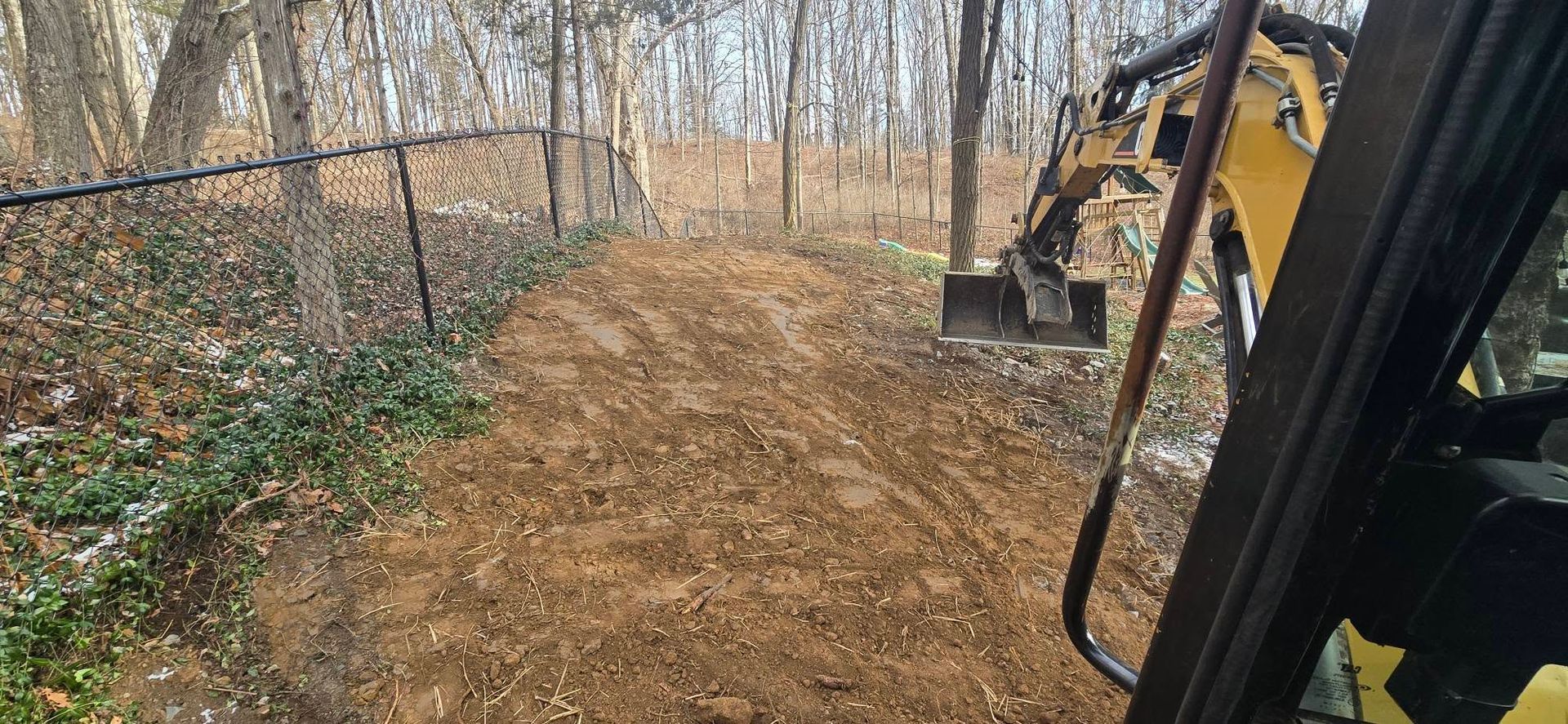 A yellow excavator is digging a path in the woods.
