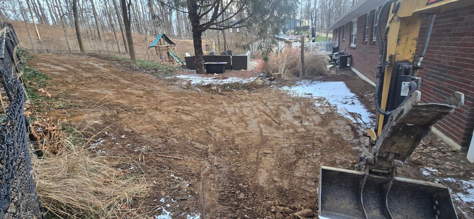 A bulldozer is moving dirt in a yard next to a brick building.