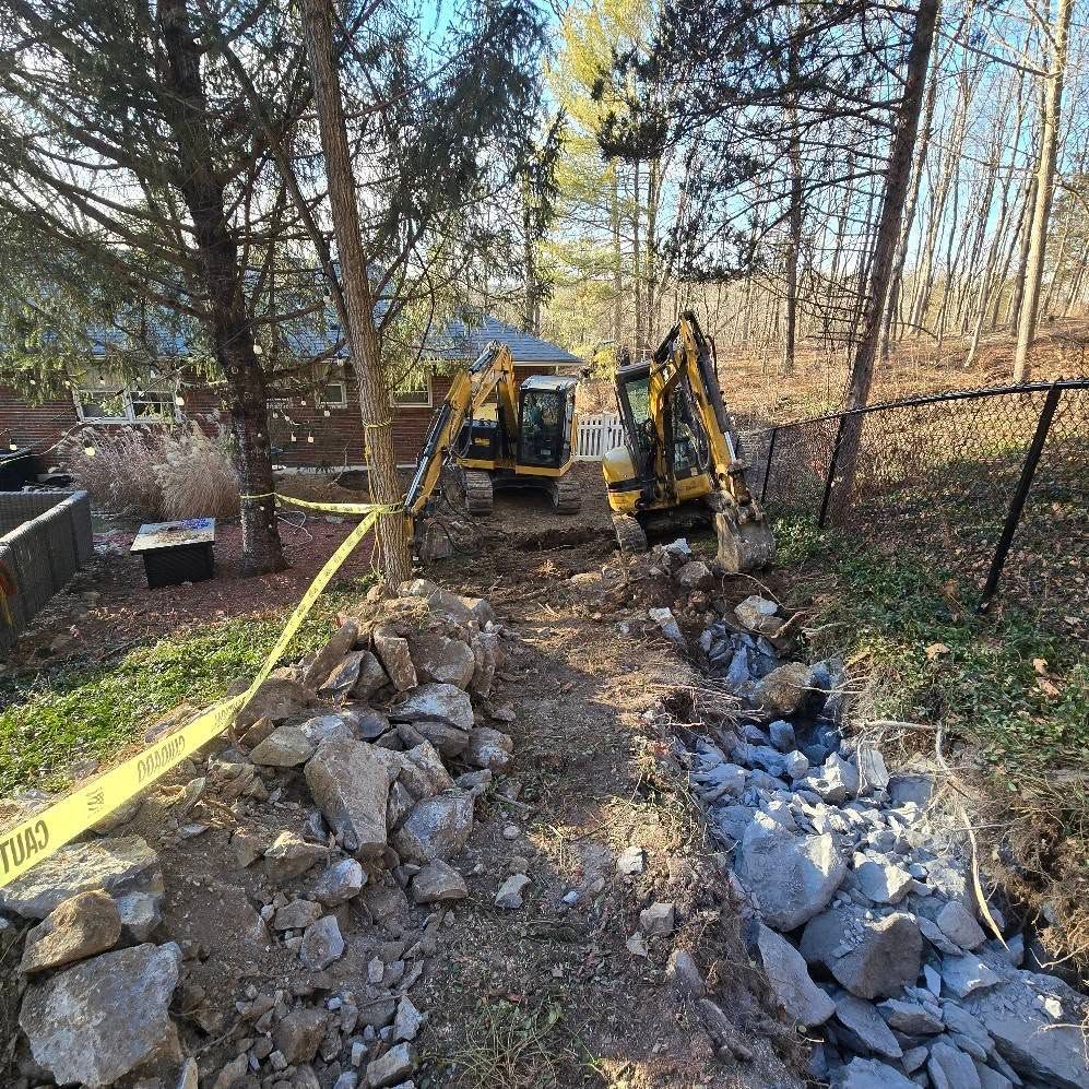 A couple of excavators are working on a rocky area in the woods.