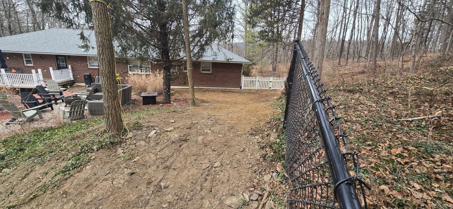 A chain link fence surrounds a dirt road leading to a house in the woods.