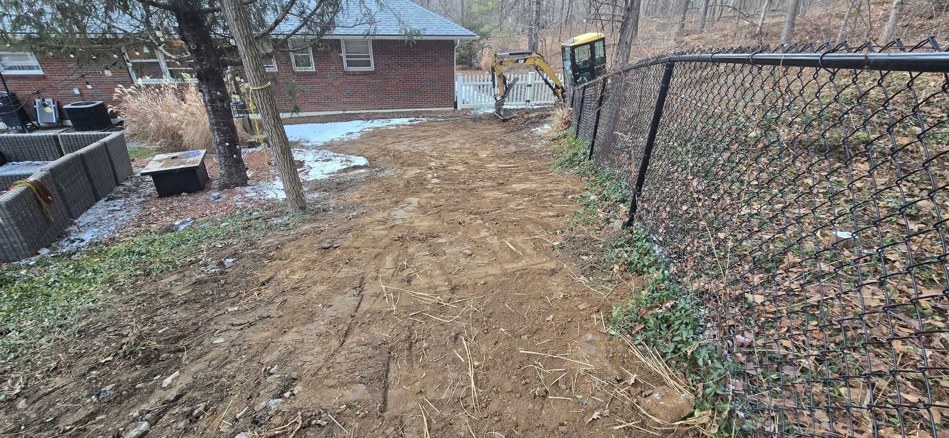 A dirt road with a chain link fence and a house in the background.