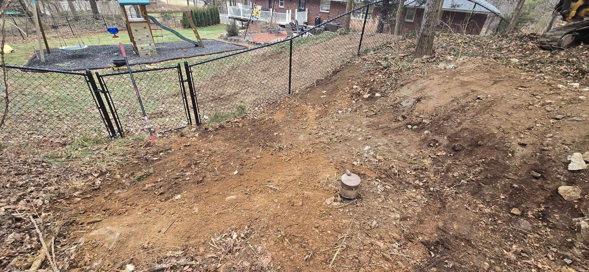 A dirt field with a chain link fence and a swing set in the background.