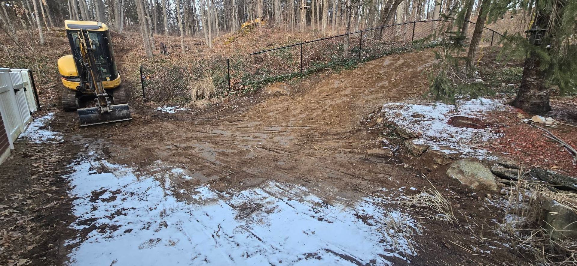 A yellow excavator is digging a hole in the mud in the woods.