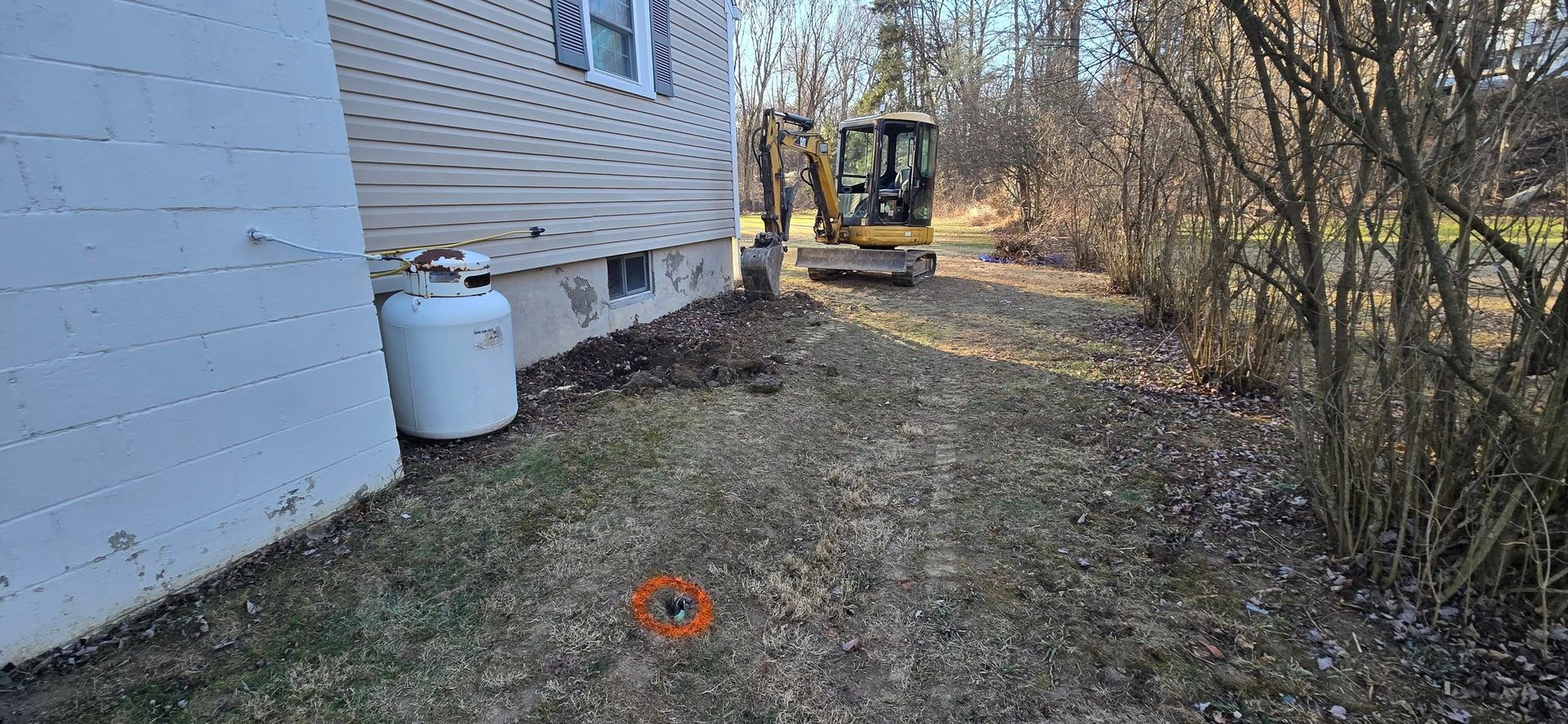 A yellow excavator is digging a hole in the ground in front of a house.