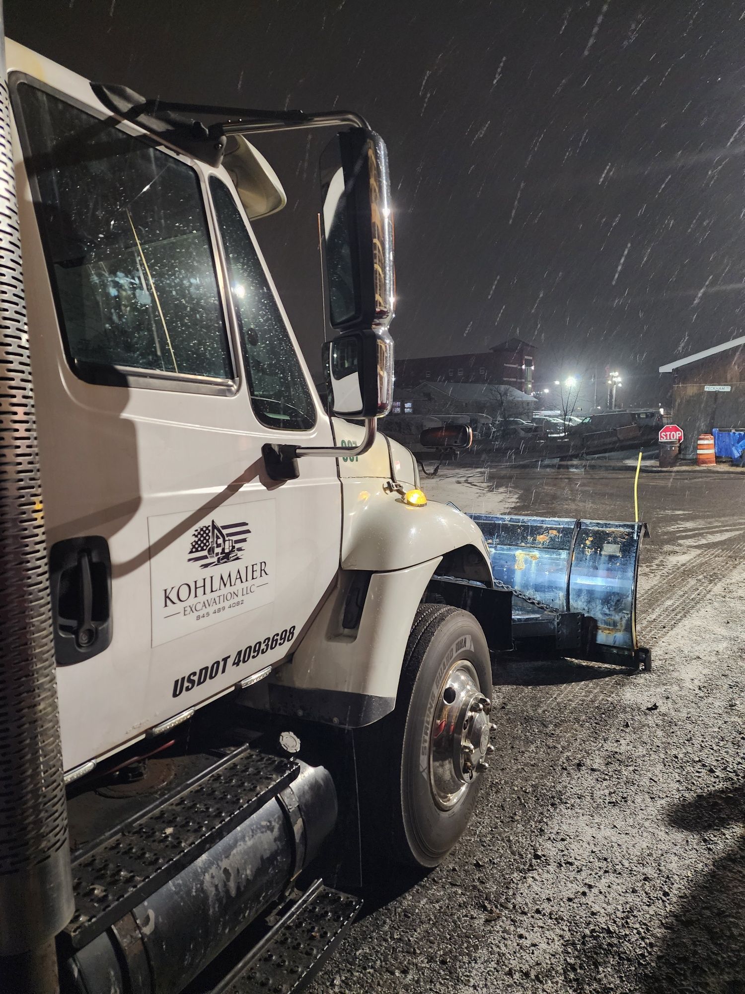 A snow plow is parked in a parking lot at night.