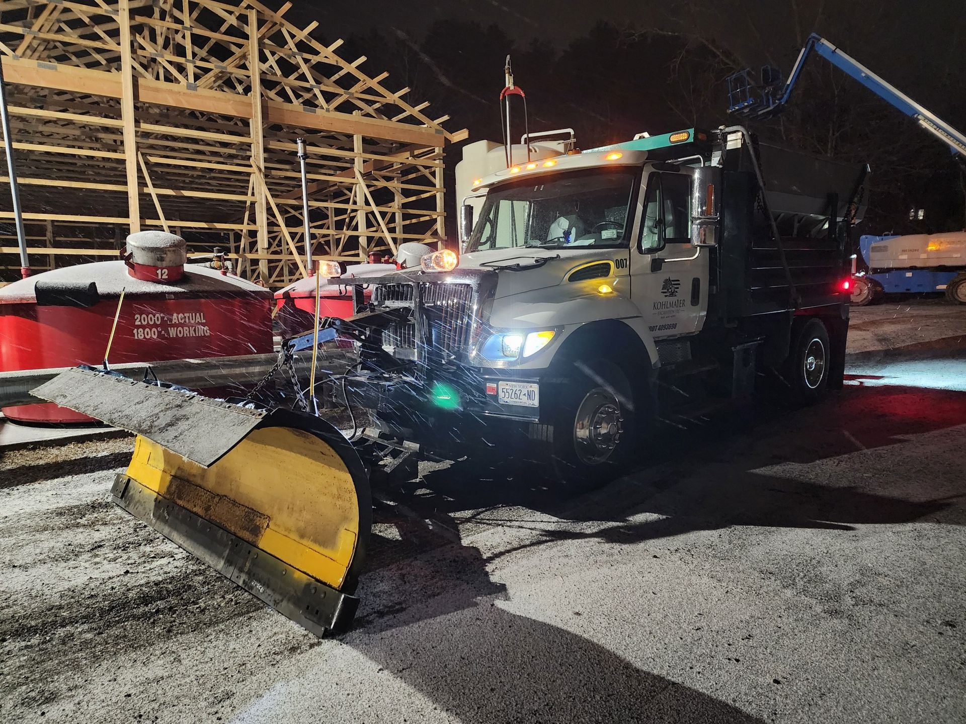 A snow plow is parked in front of a building at night.