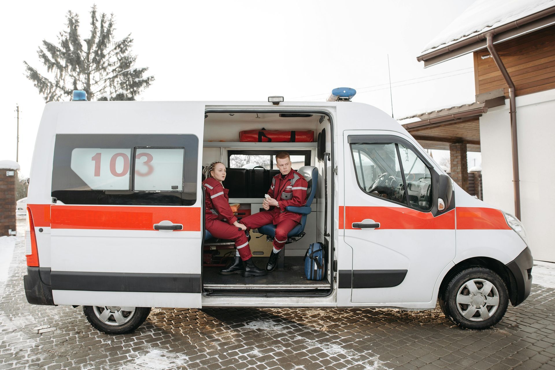 Two paramedics are sitting in an ambulance with their doors open.