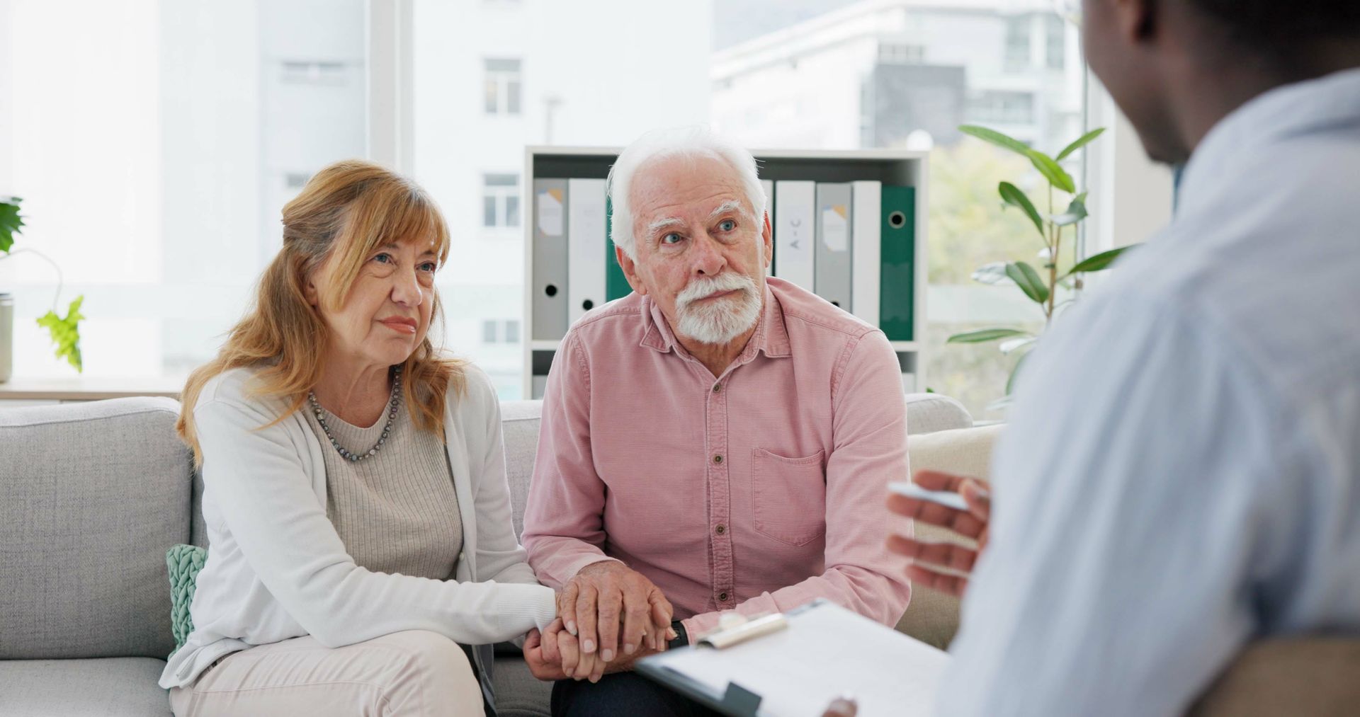 Couple speaking with a counselor in a bright office, holding hands and listening attentively.