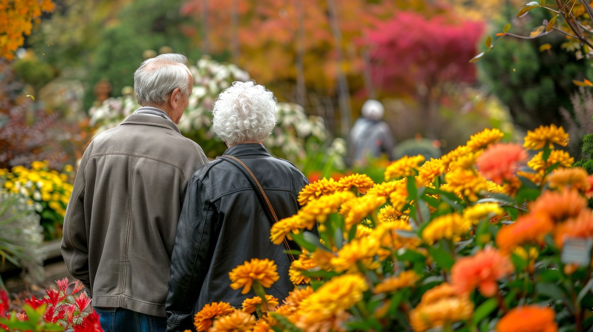 An elderly couple is walking through a garden filled with flowers.
