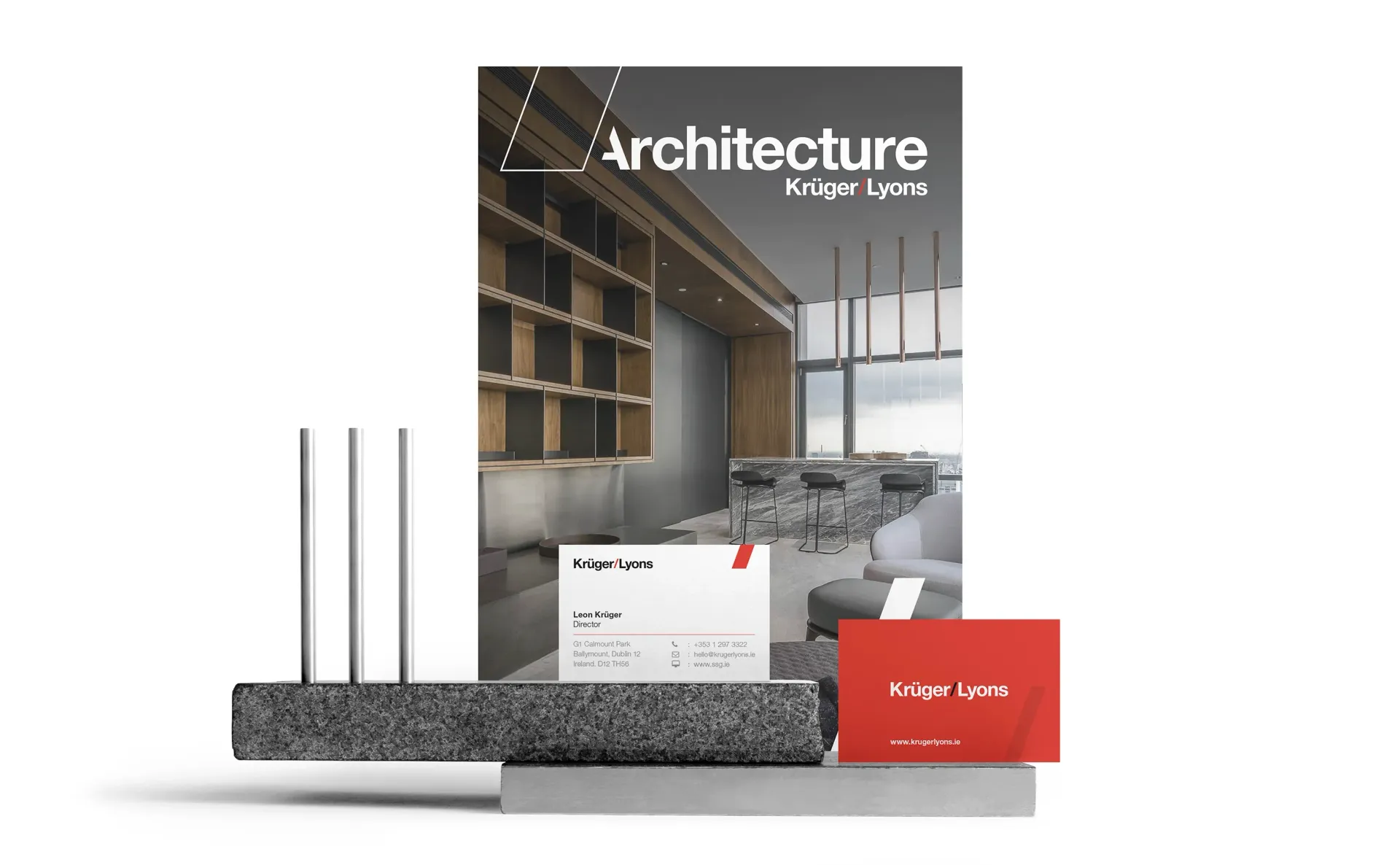 Magazine cover with business cards and metal rods on a gray block, likely for architectural firm promotion.