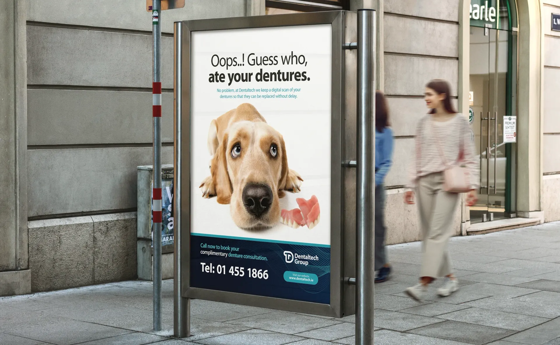 Advertisement with a sad-eyed dog beside dentures; two people walk past the billboard on a city sidewalk.