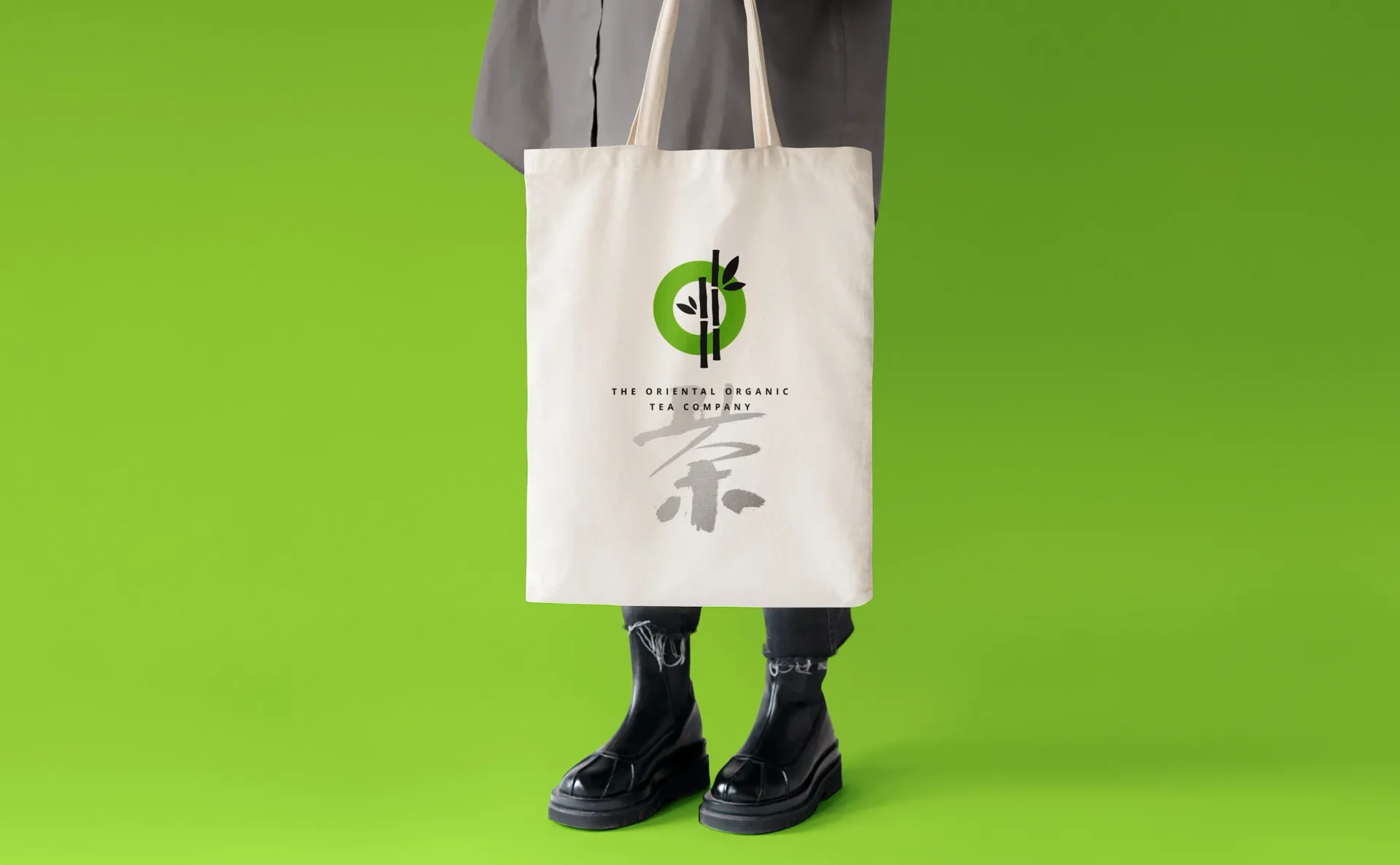 Person holding a canvas tote bag with a bamboo logo against a lime green backdrop.